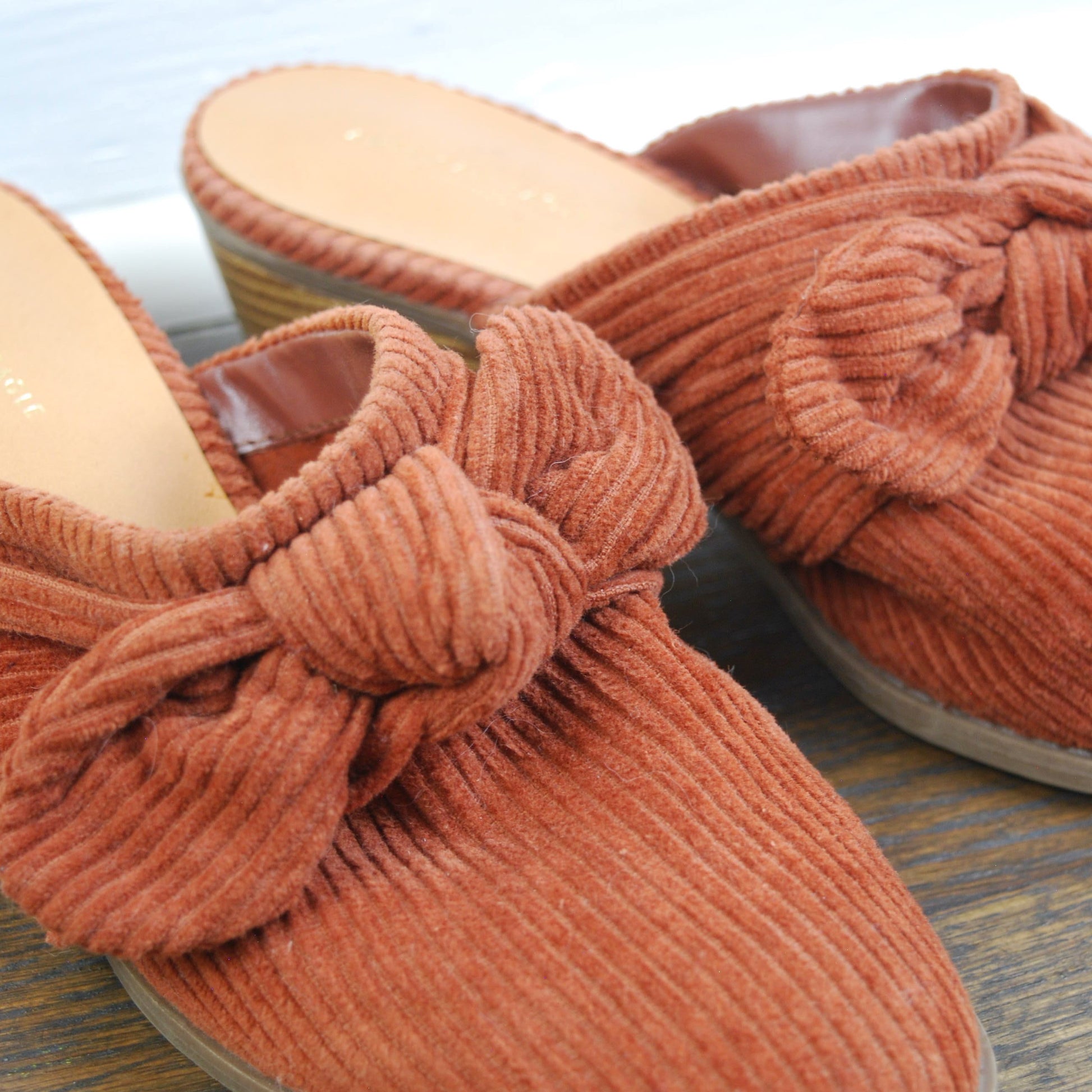Pair of orange slippers with knotted design on a wooden surface