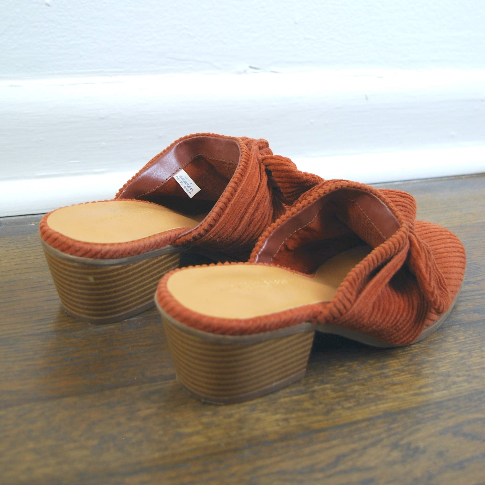 Pair of orange sandals on a wooden floor with a white wall background