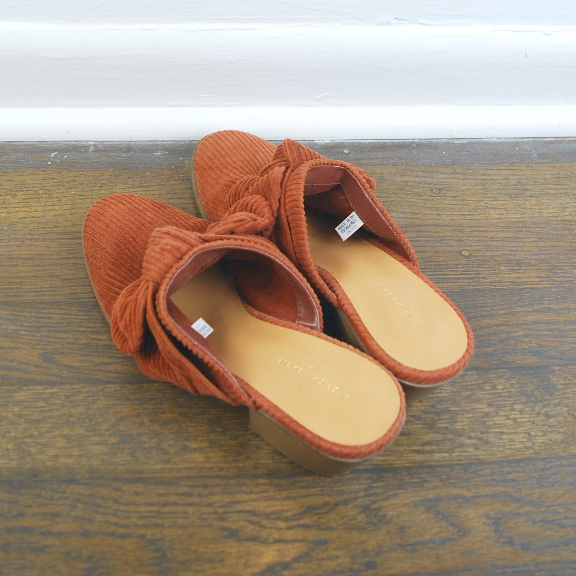 Pair of brown slippers with a bow on a wooden floor.