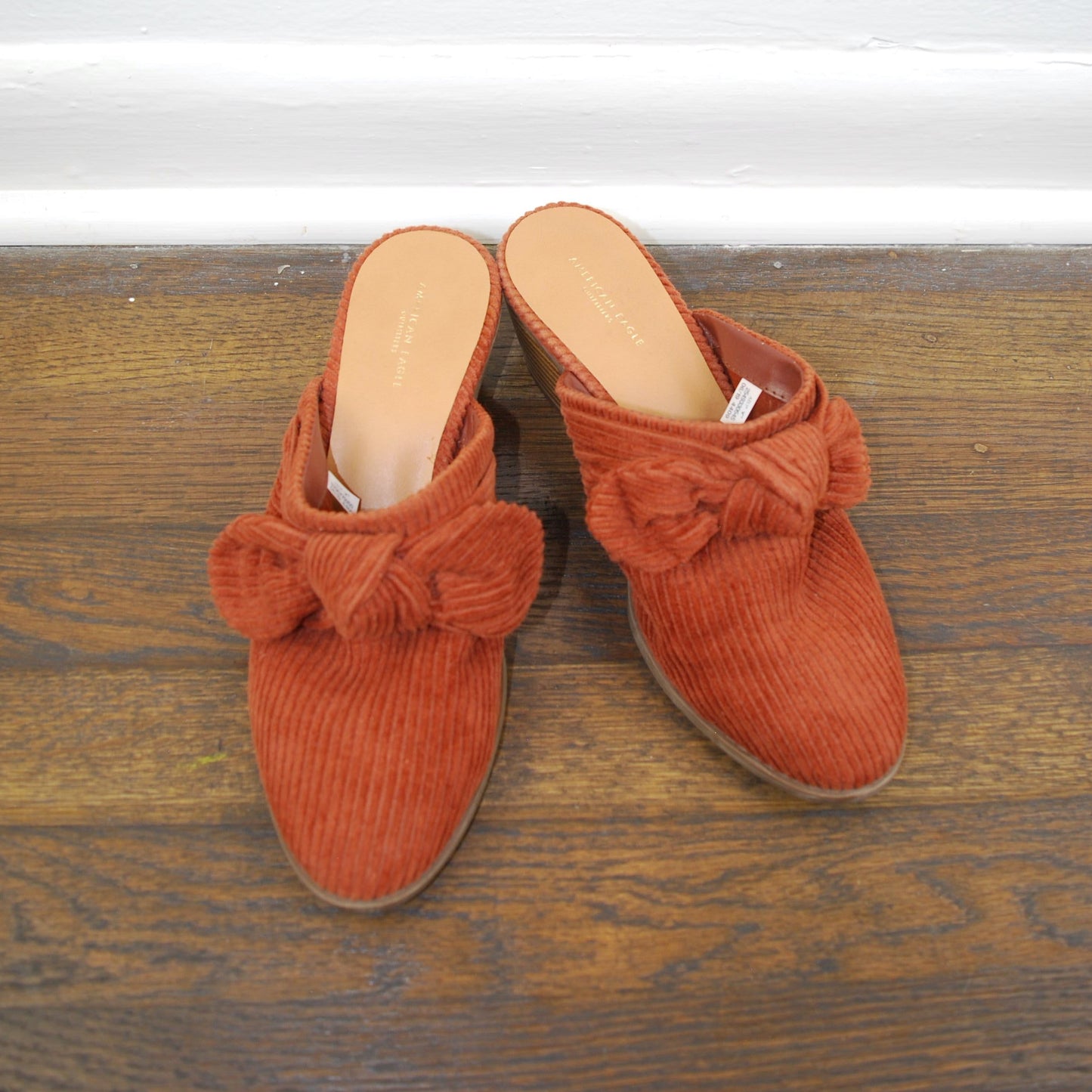 Pair of orange slippers with bow details on a wooden floor.