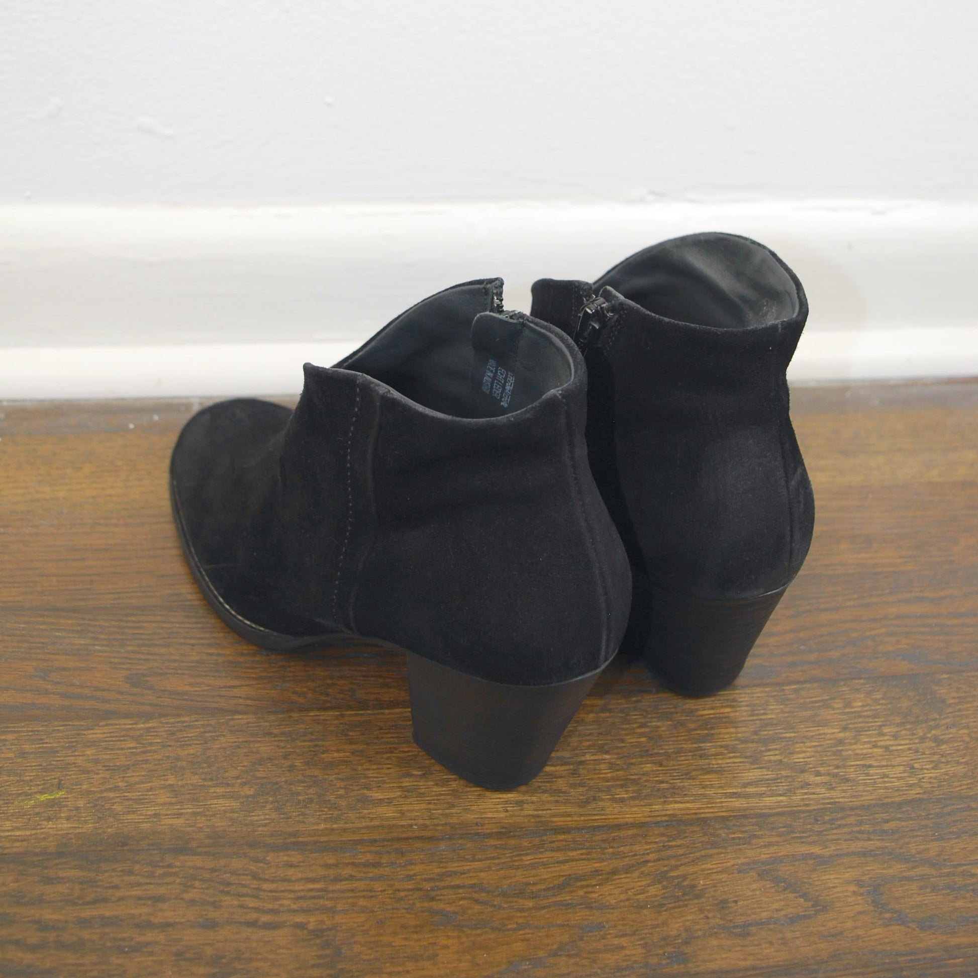 Pair of black ankle boots on a wooden floor with a white baseboard.