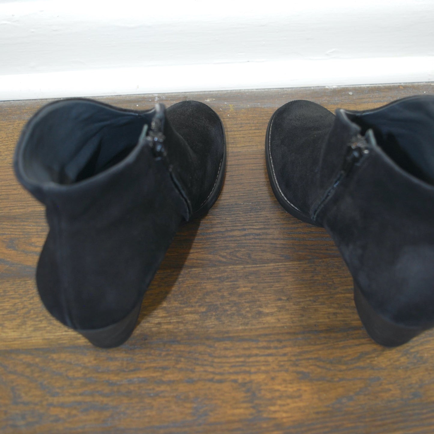 Pair of black suede boots on a wooden floor with a white baseboard.