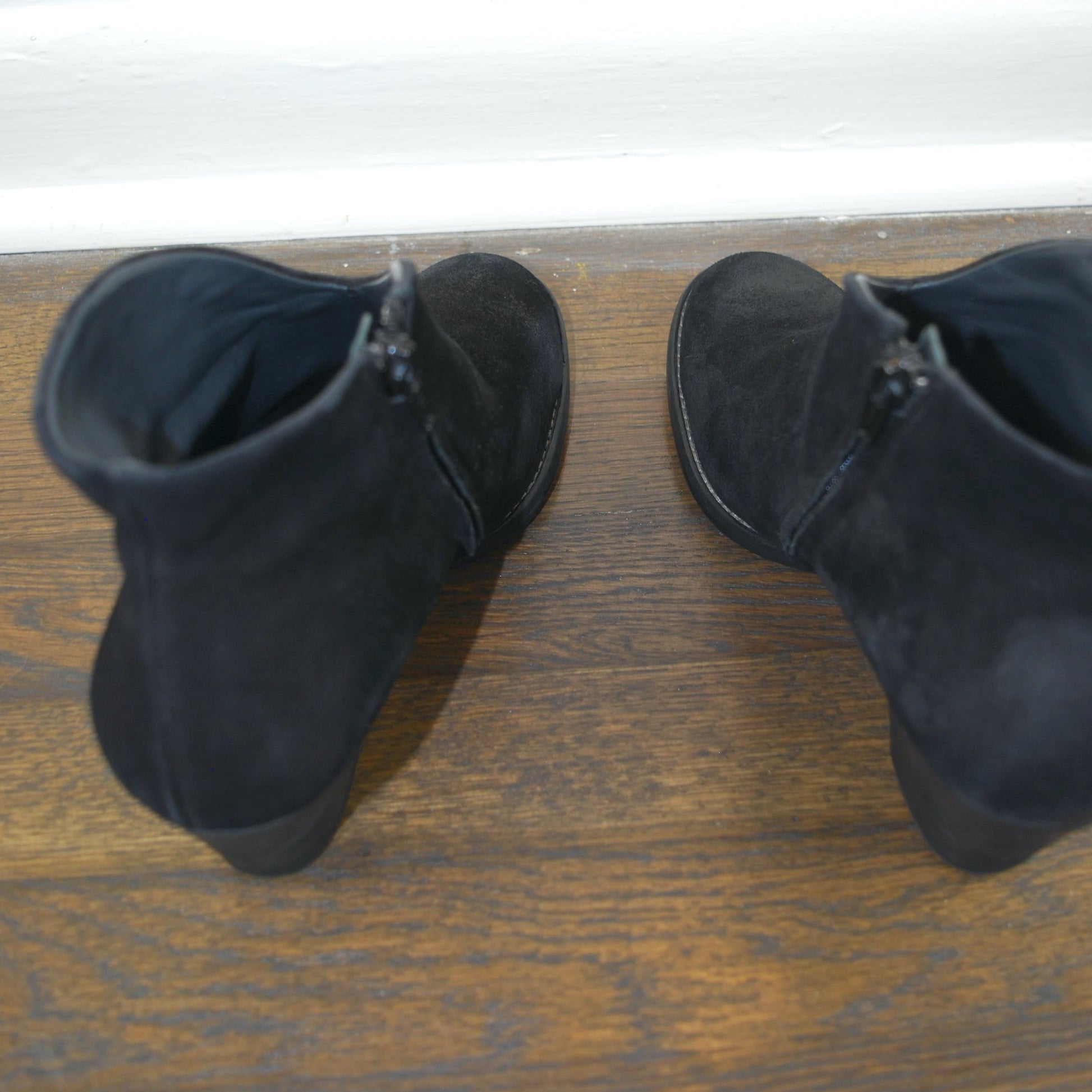 Pair of black suede boots on a wooden floor with a white baseboard.