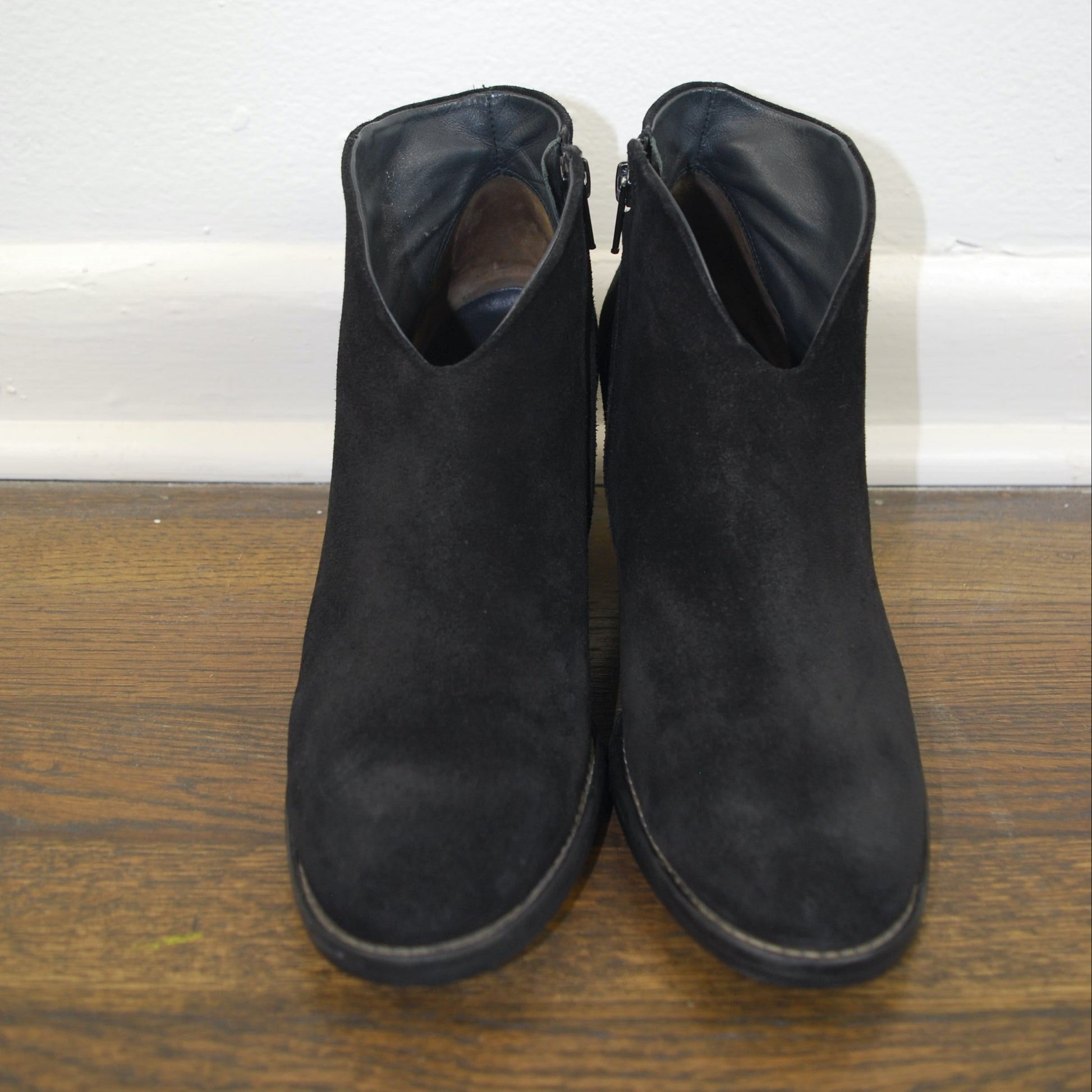 Pair of black ankle boots on a wooden floor with a white baseboard.