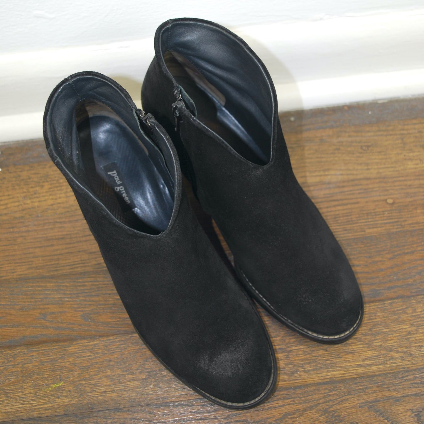 Pair of black ankle boots on a wooden floor with a white baseboard.