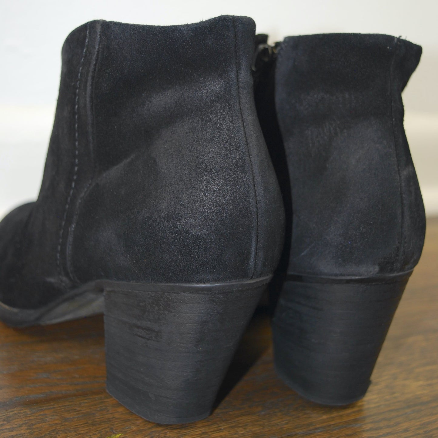Pair of black suede ankle boots on a wooden surface with a white background