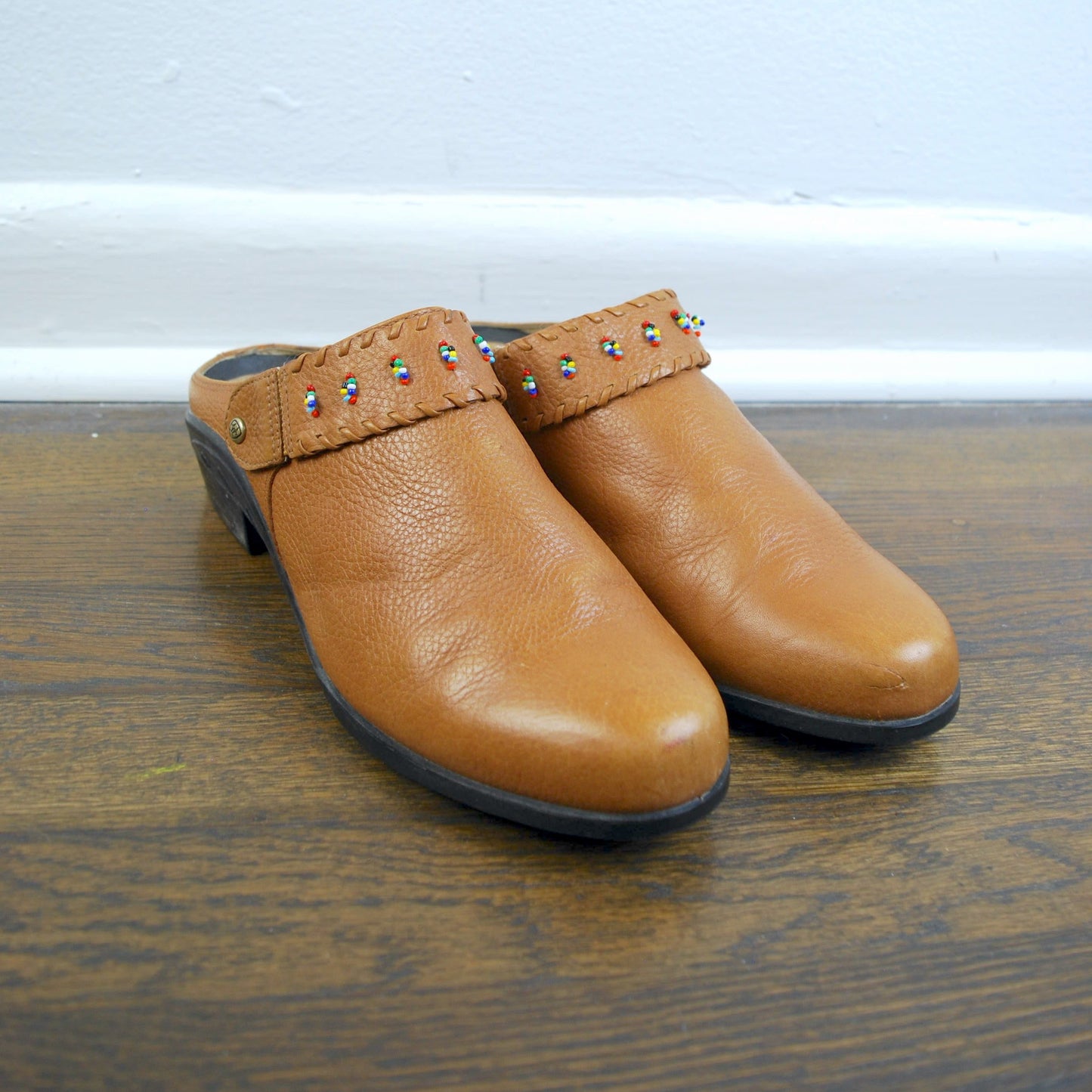 Pair of tan clogs with decorative studs on a wooden floor.