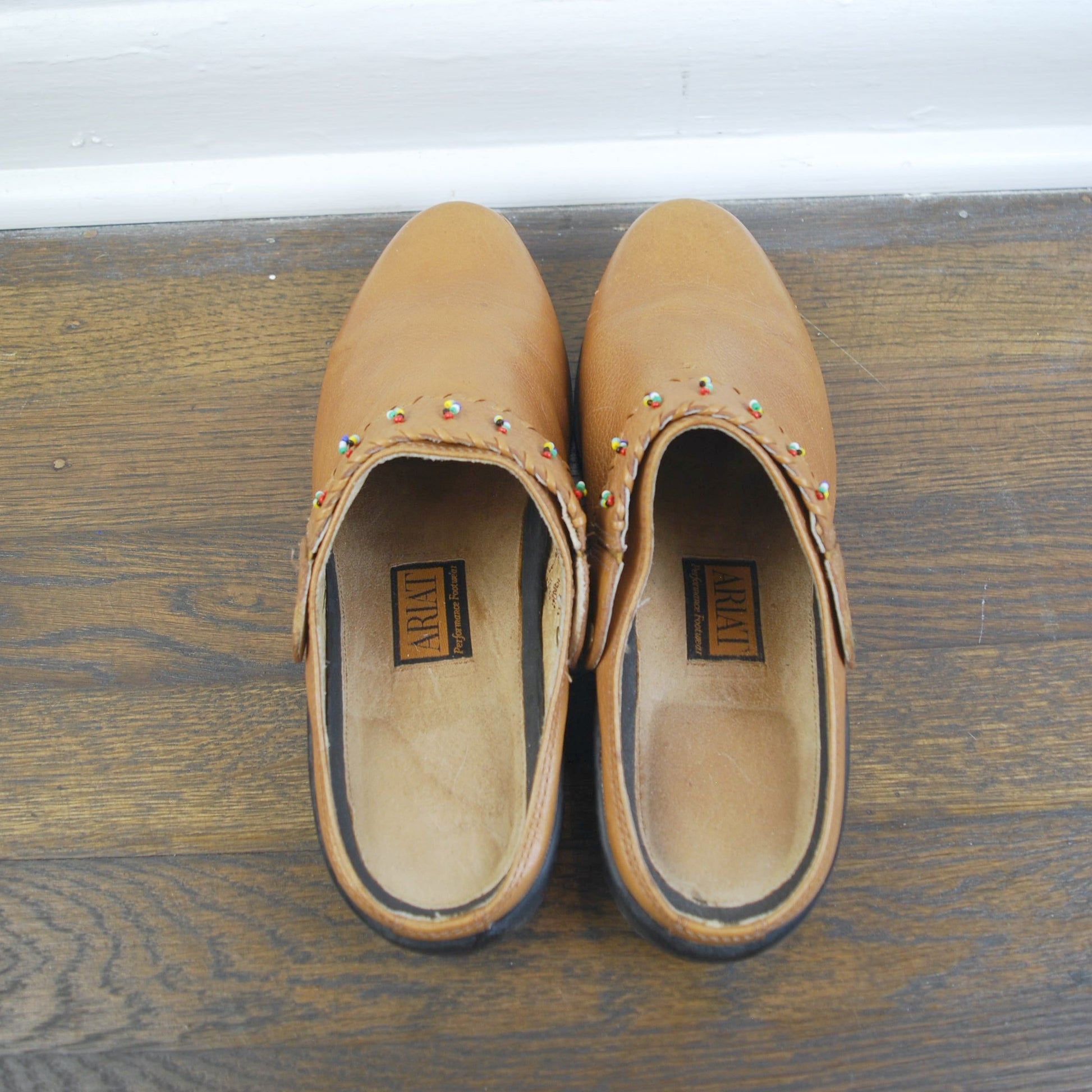 Pair of tan clogs with studs on a wooden floor.
