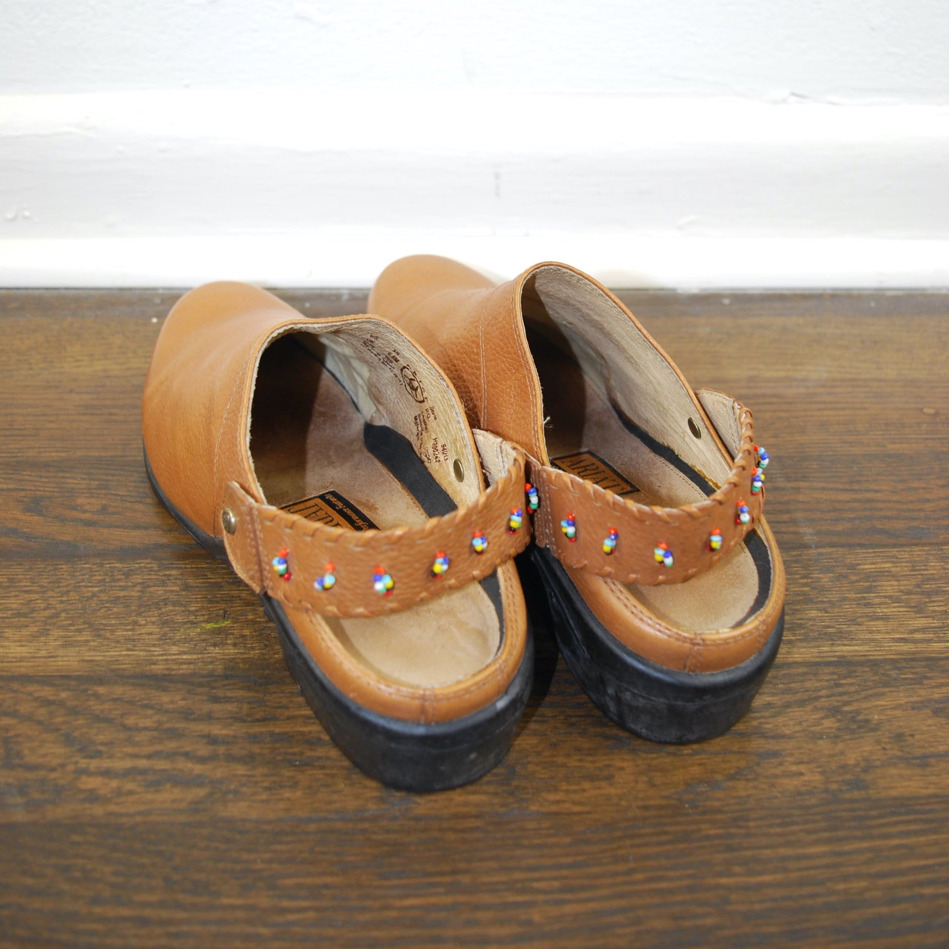 Pair of brown sandals with decorative straps on a wooden surface