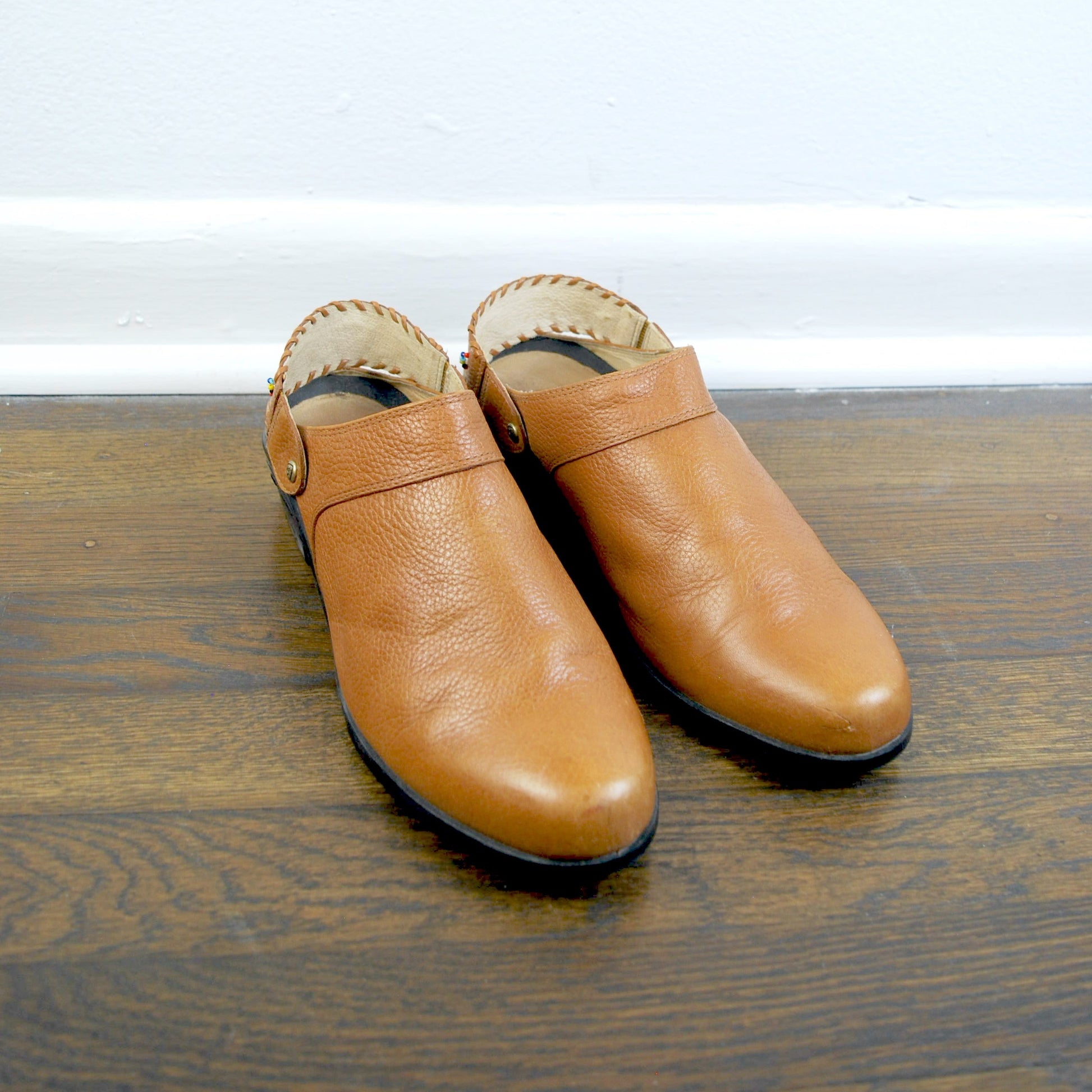 Pair of tan leather shoes on a wooden surface with a white background