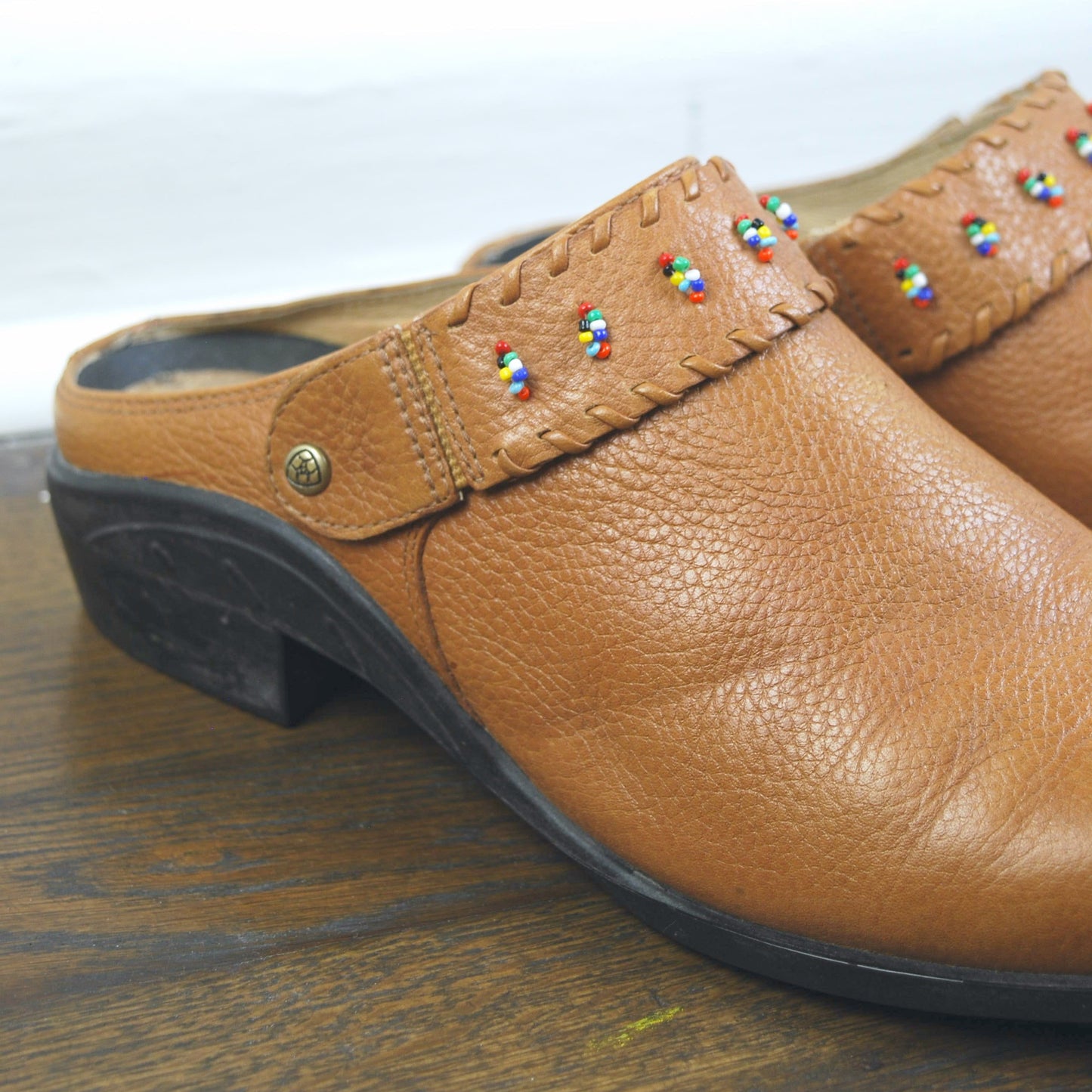 Brown leather clog shoe with colorful embellishments on a wooden surface.