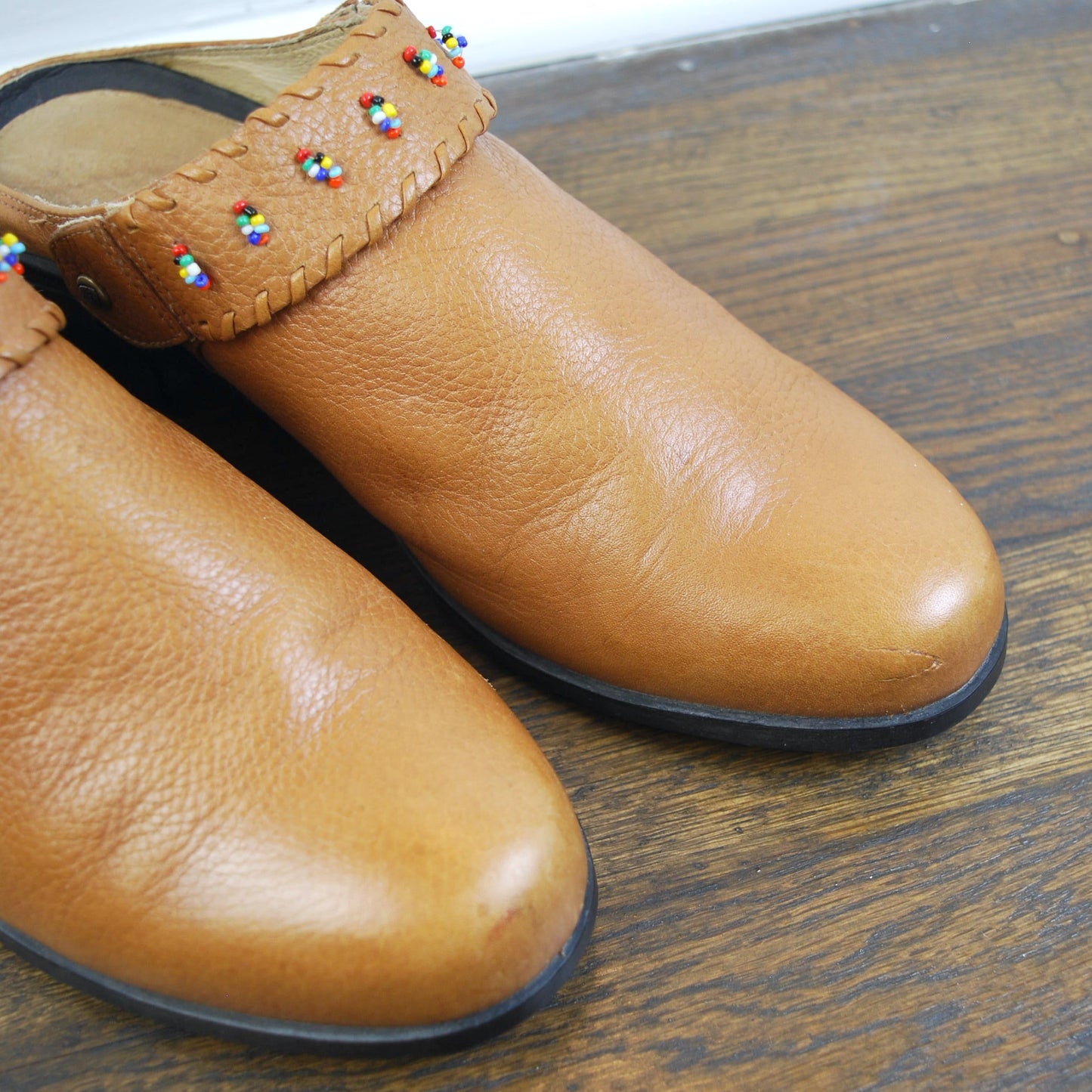 Pair of tan leather shoes with decorative trim on a wooden floor.