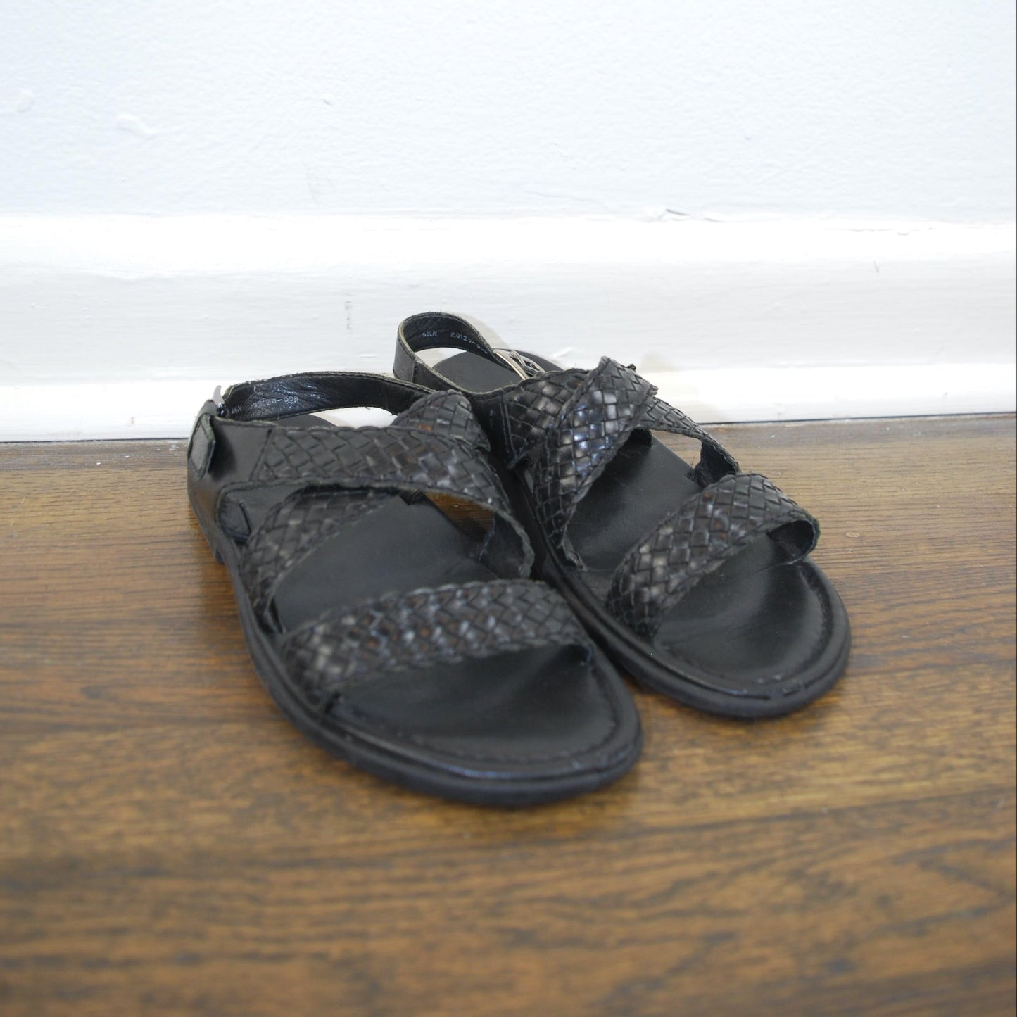 Pair of black sandals on a wooden floor with a white wall background