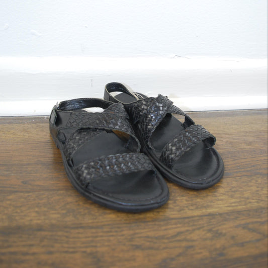 Pair of black sandals on a wooden floor with a white wall background