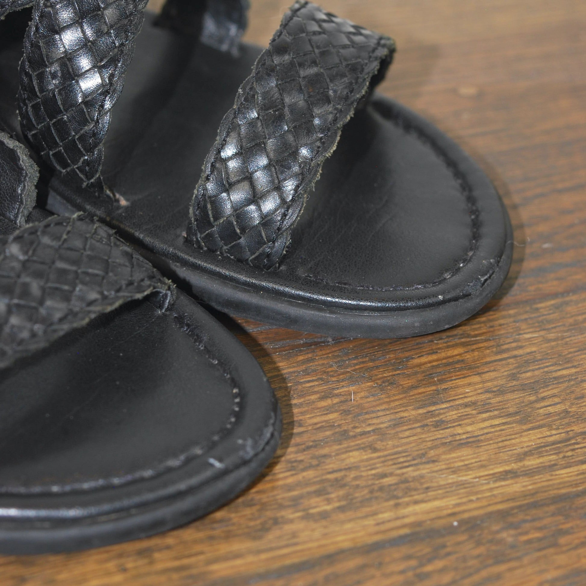 Black woven sandals on a wooden surface