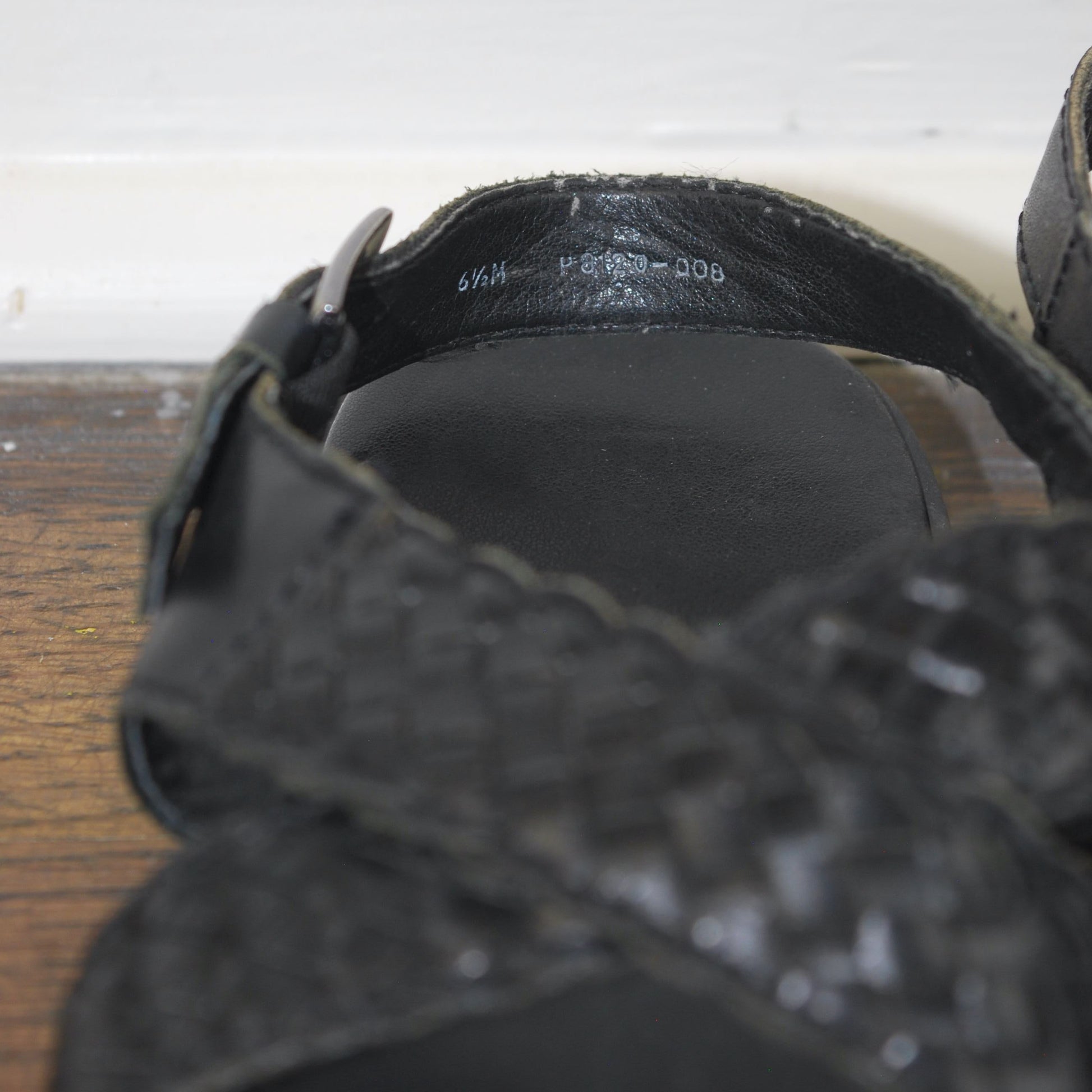 Close-up of black sandals with a visible brand logo on a white and wooden surface.