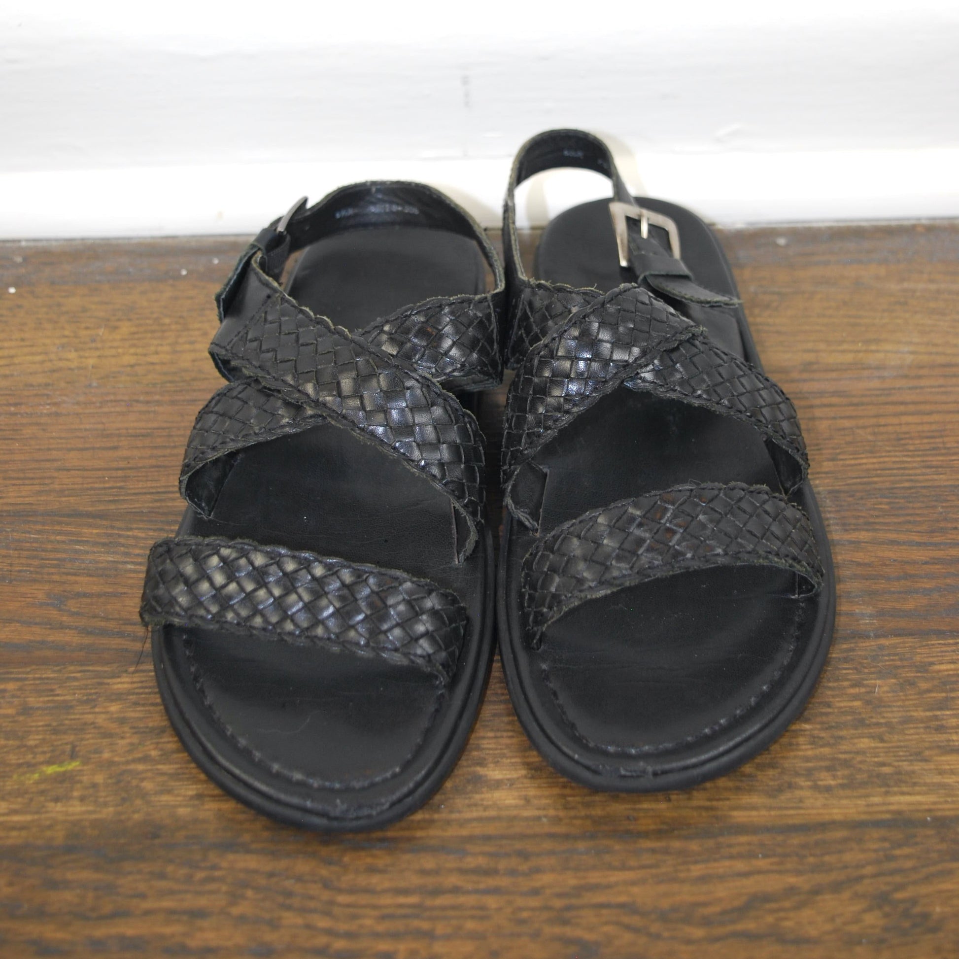 Pair of black sandals on a wooden surface with a white background