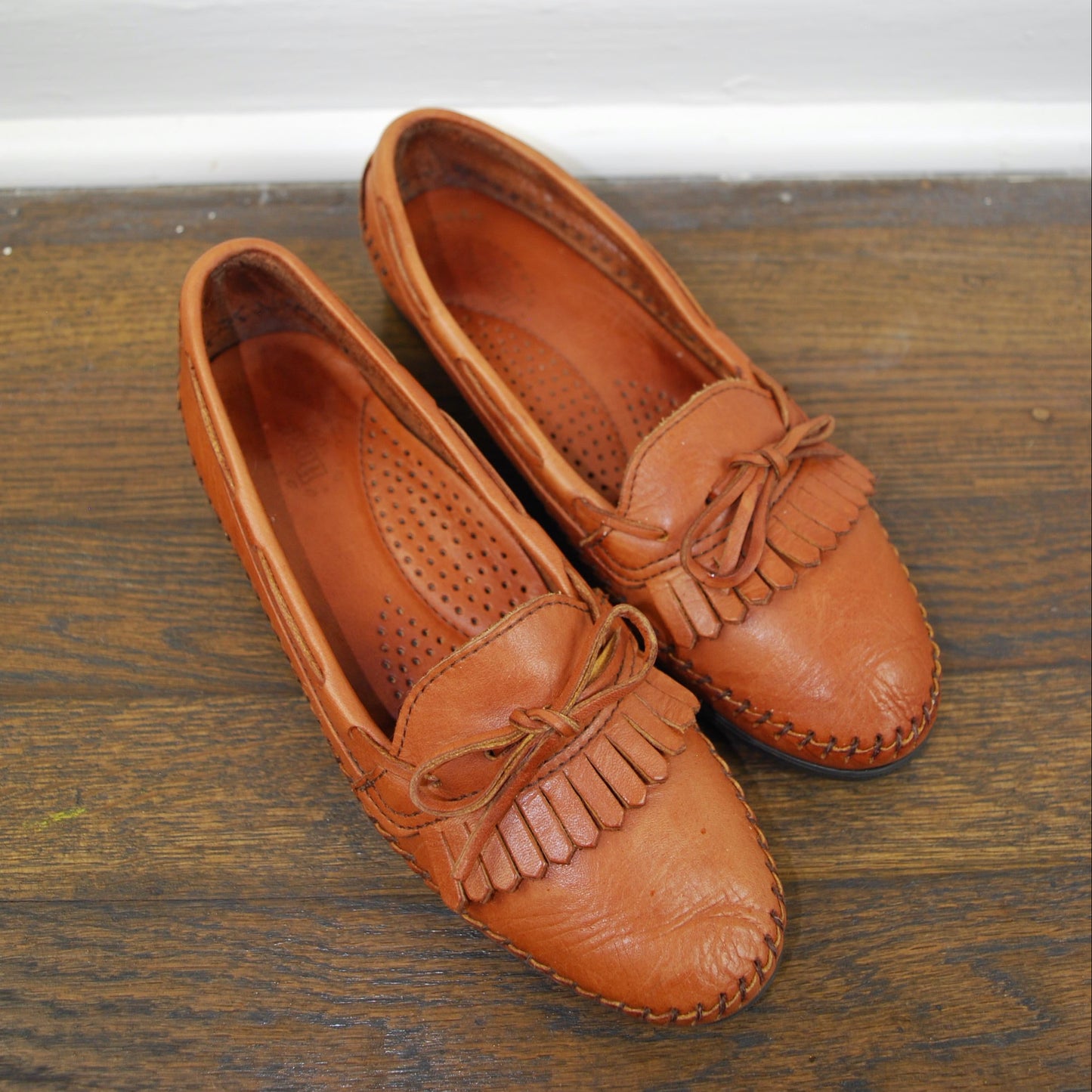 Pair of brown leather loafers with tassels on a wooden floor.