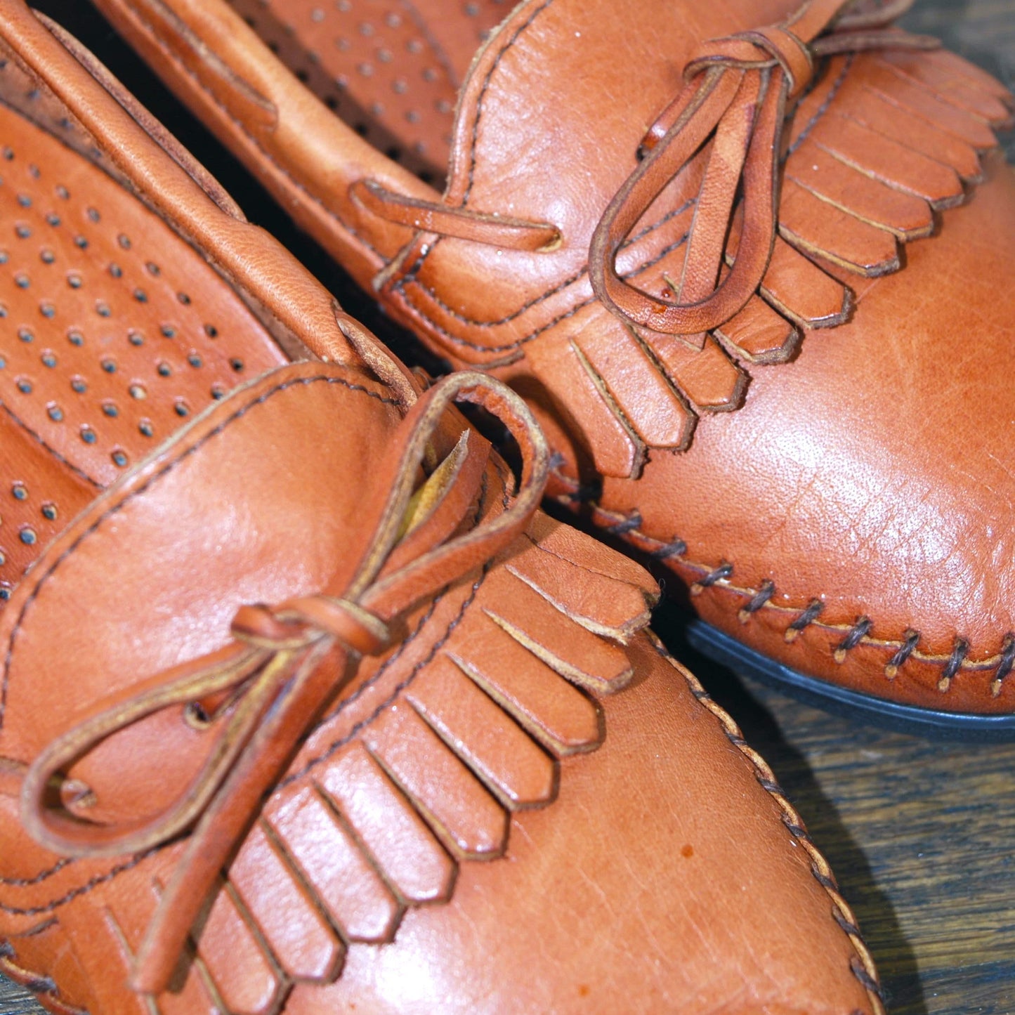 Pair of brown leather shoes with fringes on a wooden surface