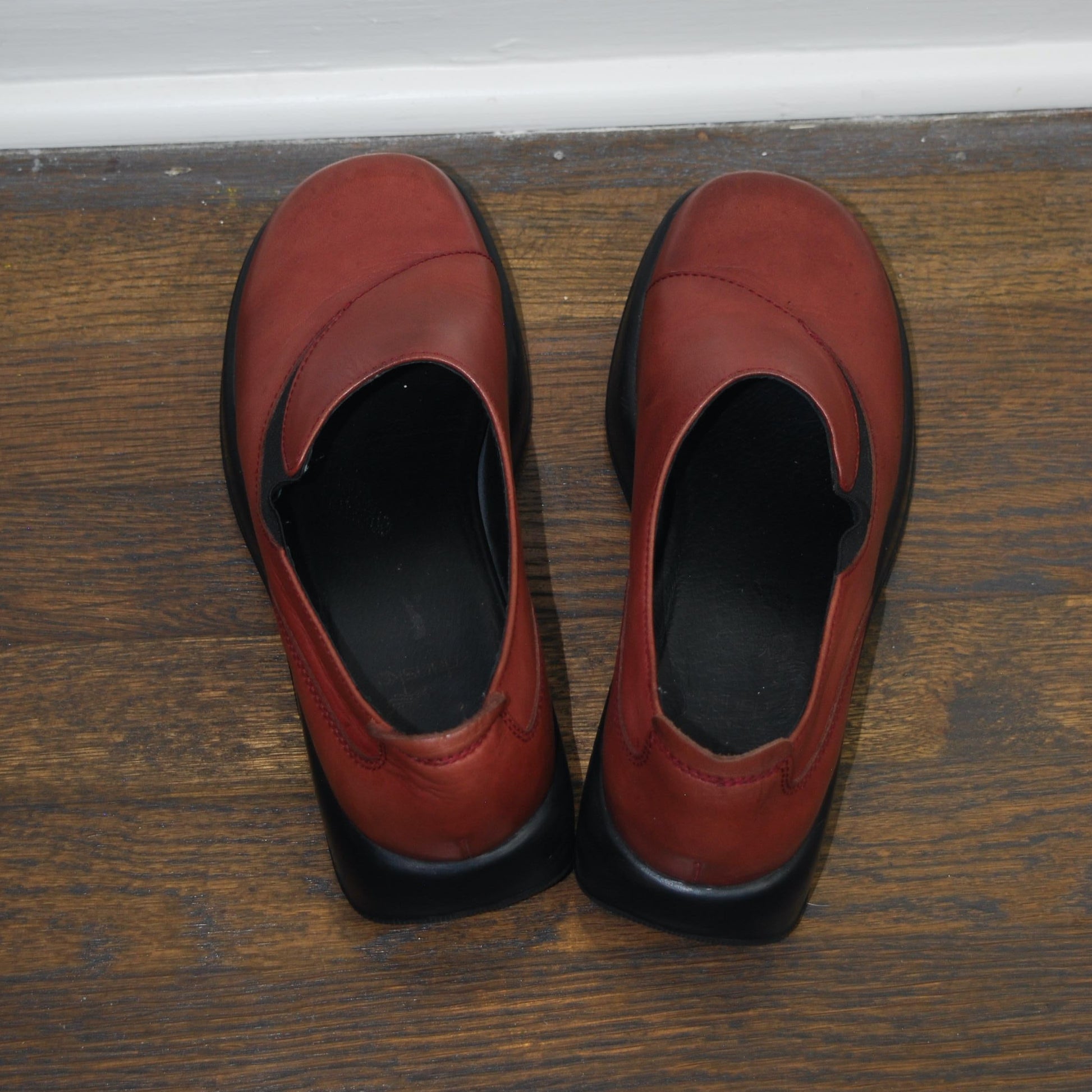 Pair of red shoes on a wooden floor with a white baseboard.