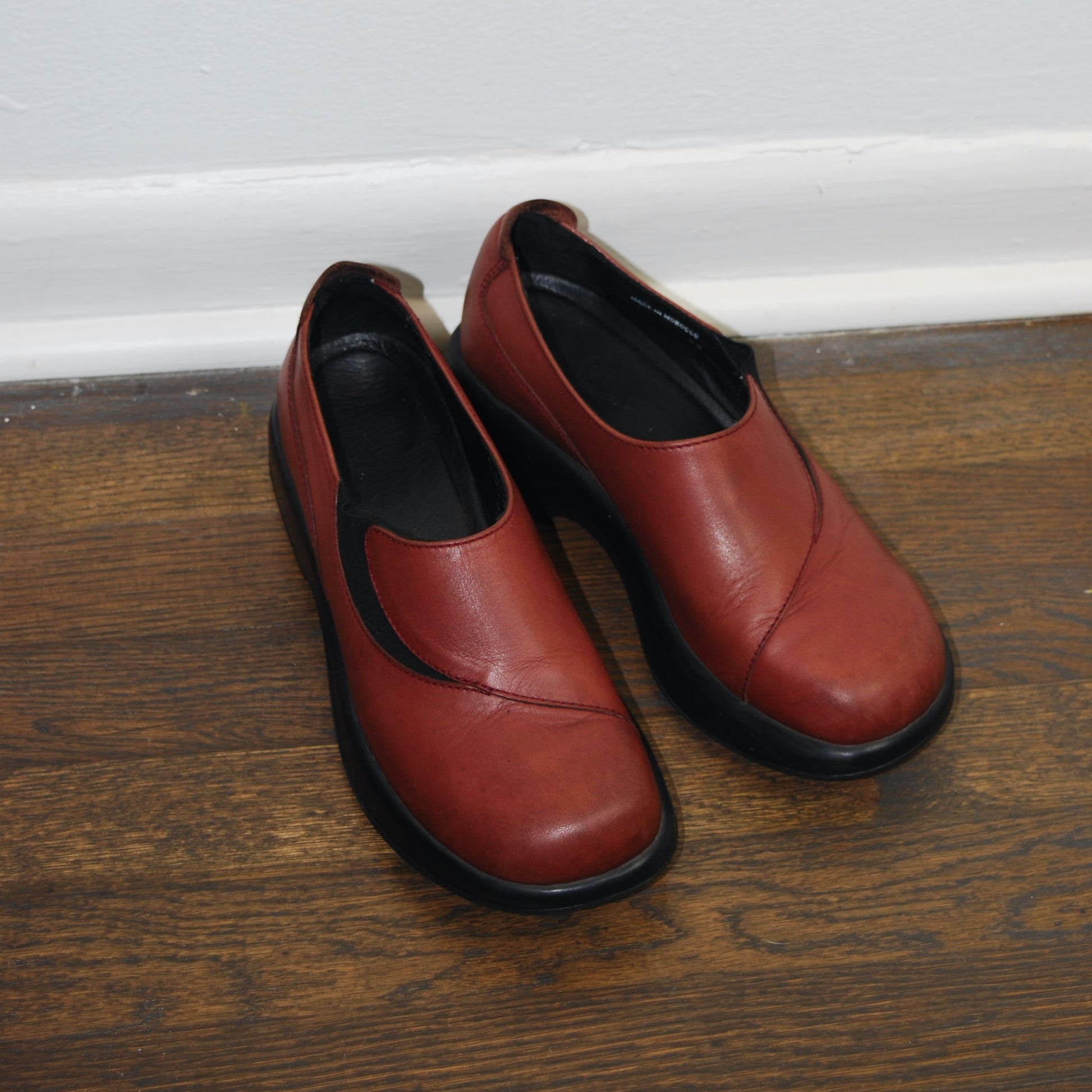 Pair of red shoes on a wooden floor against a white wall.