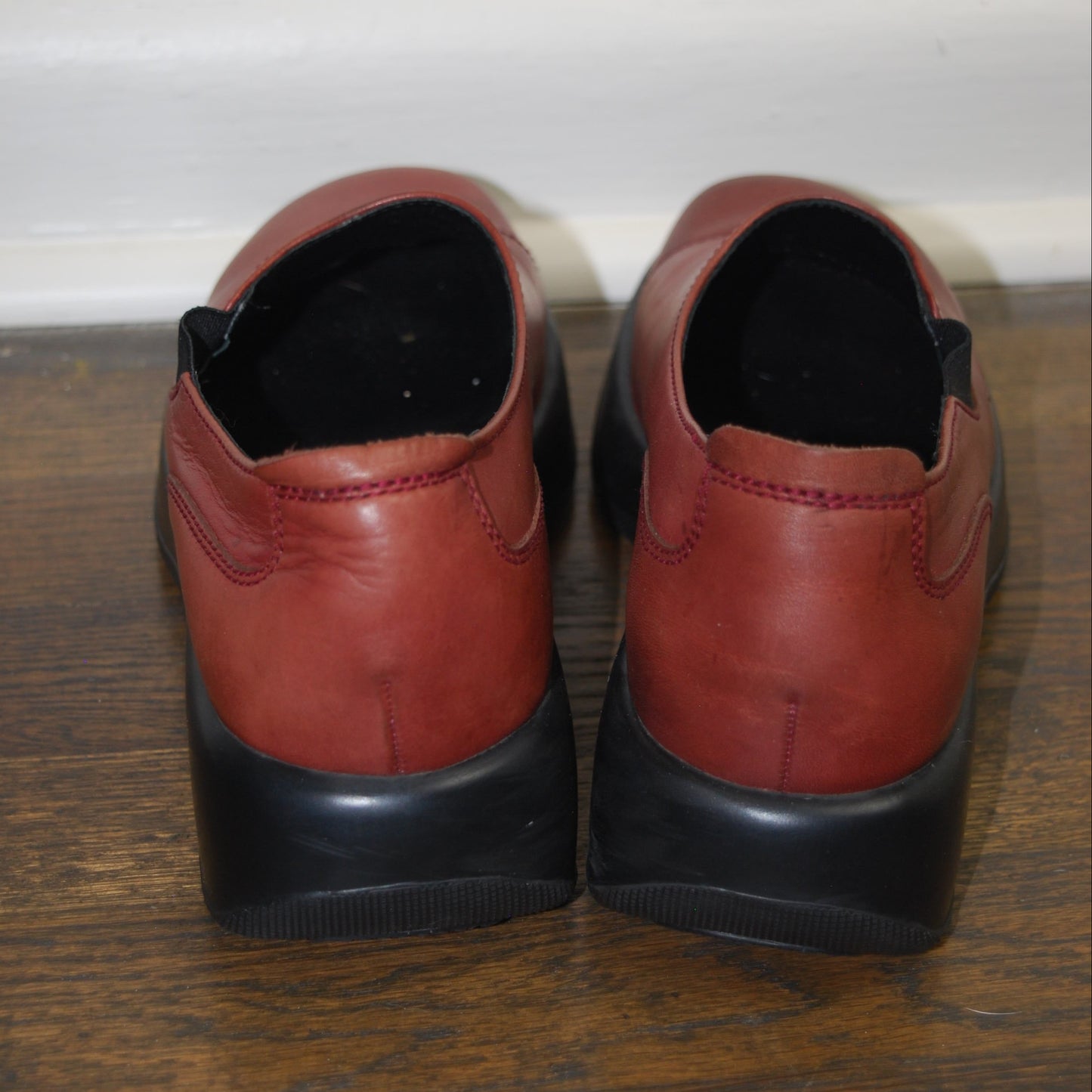 Pair of red shoes with black soles on a wooden floor.