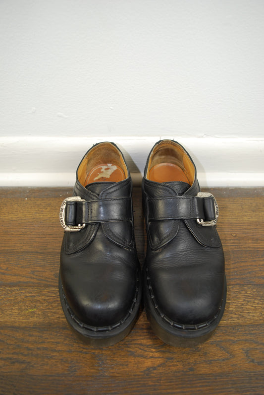 Pair of black leather shoes with buckles on a wooden floor.