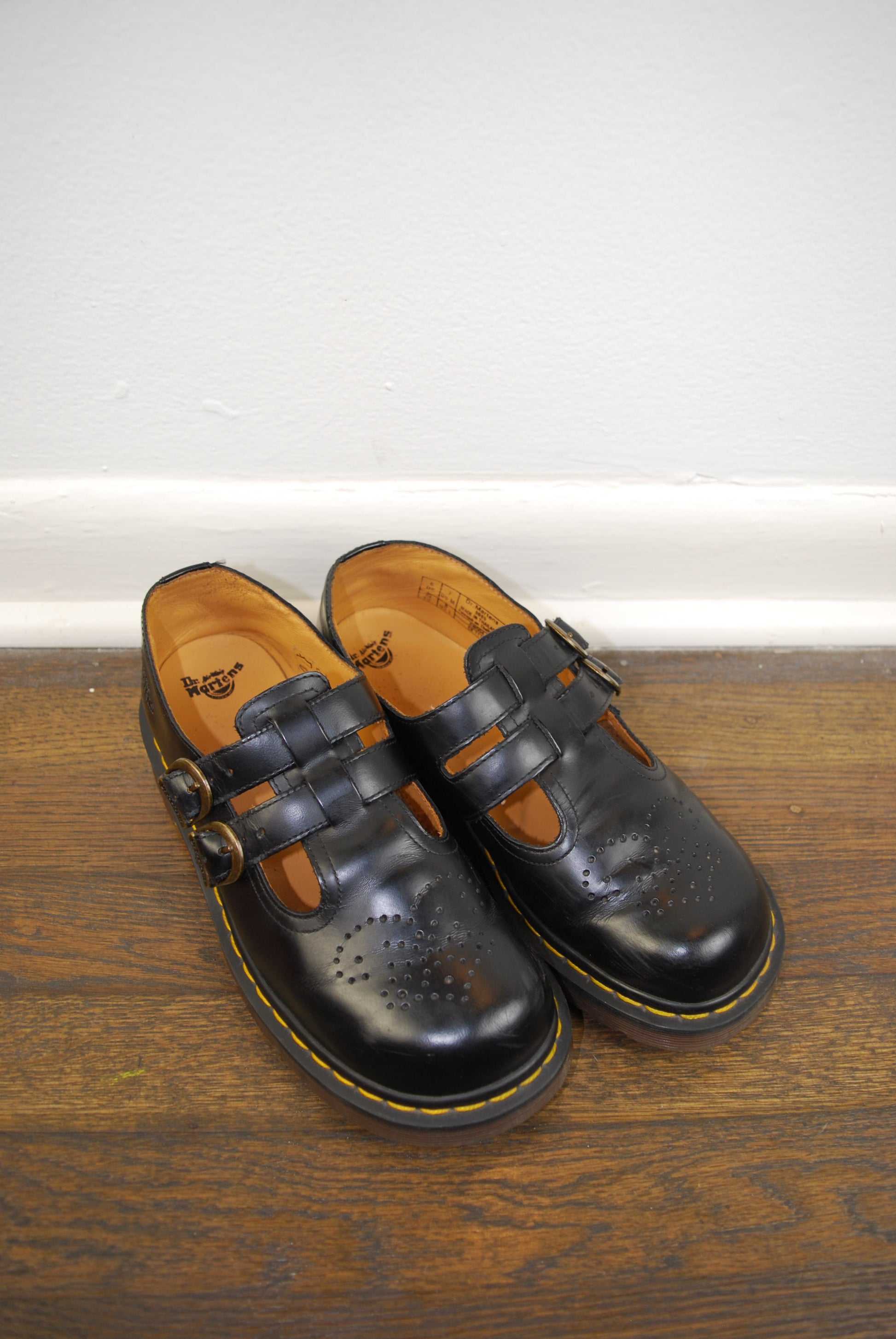 Pair of black leather shoes with brown soles on a wooden floor.