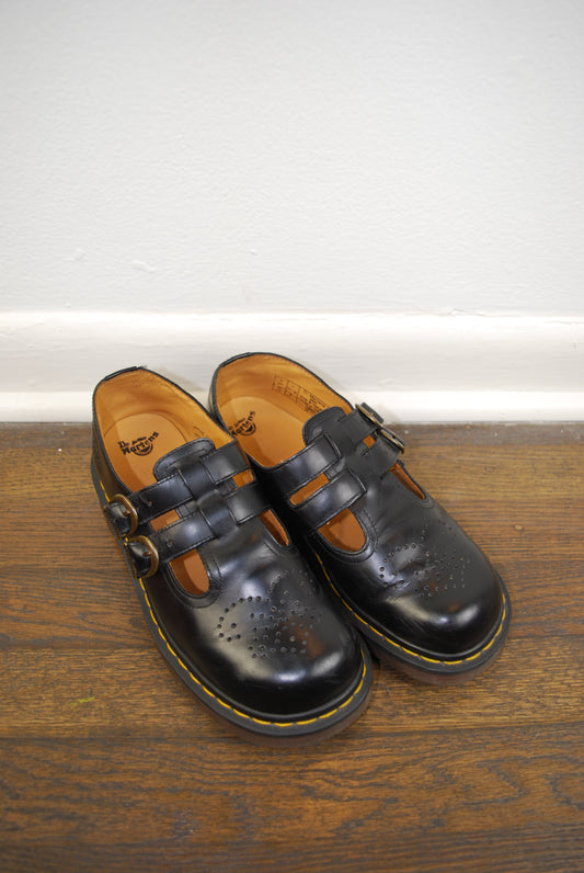 Pair of black leather shoes with brown soles on a wooden floor.
