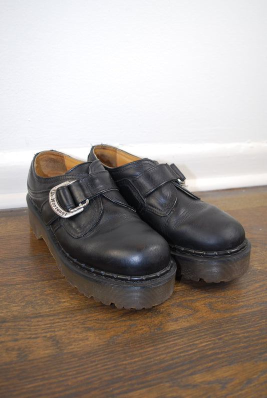Pair of black leather shoes hanging on a wooden door