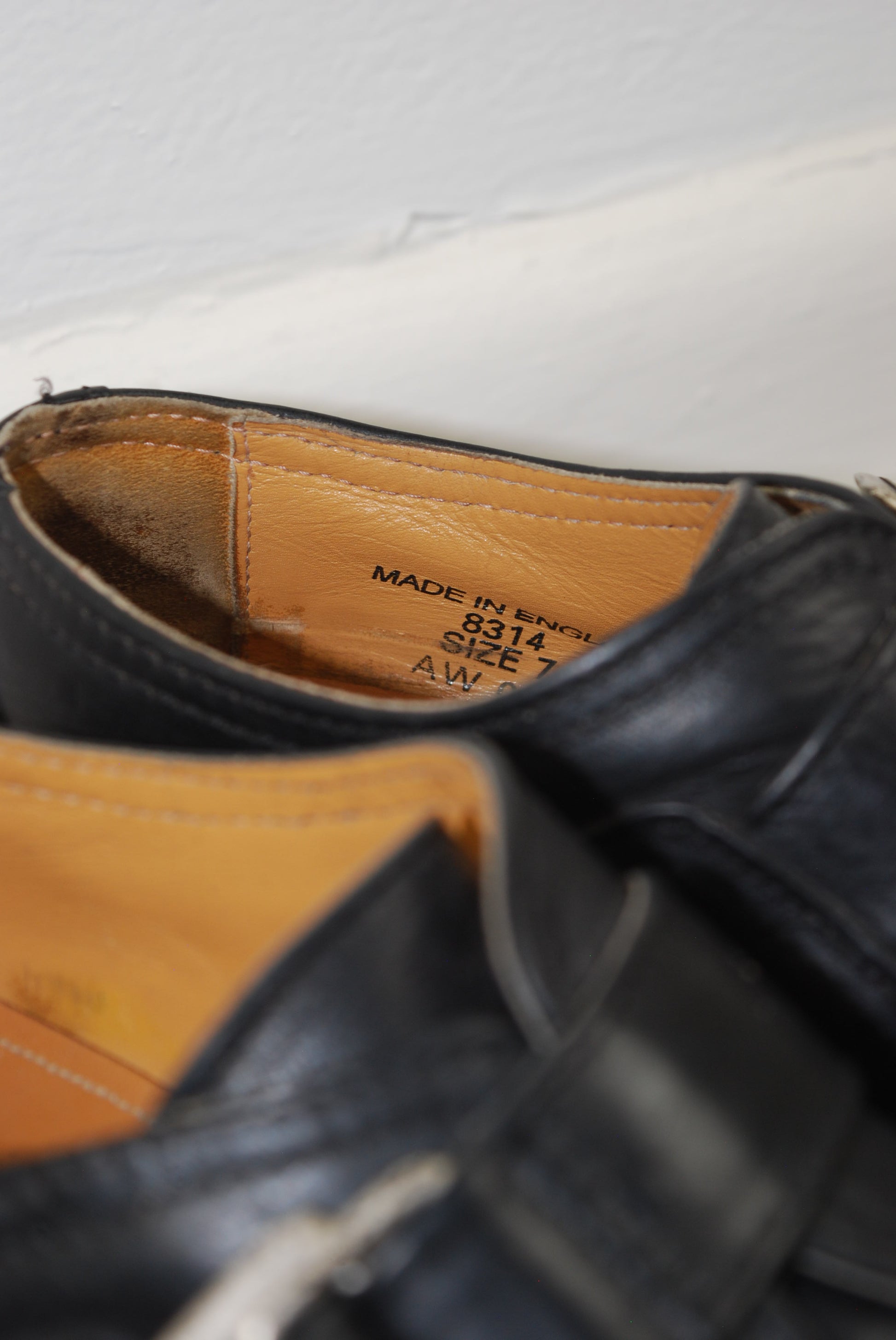 Close-up of a black leather shoe with a visible brand label on a white background