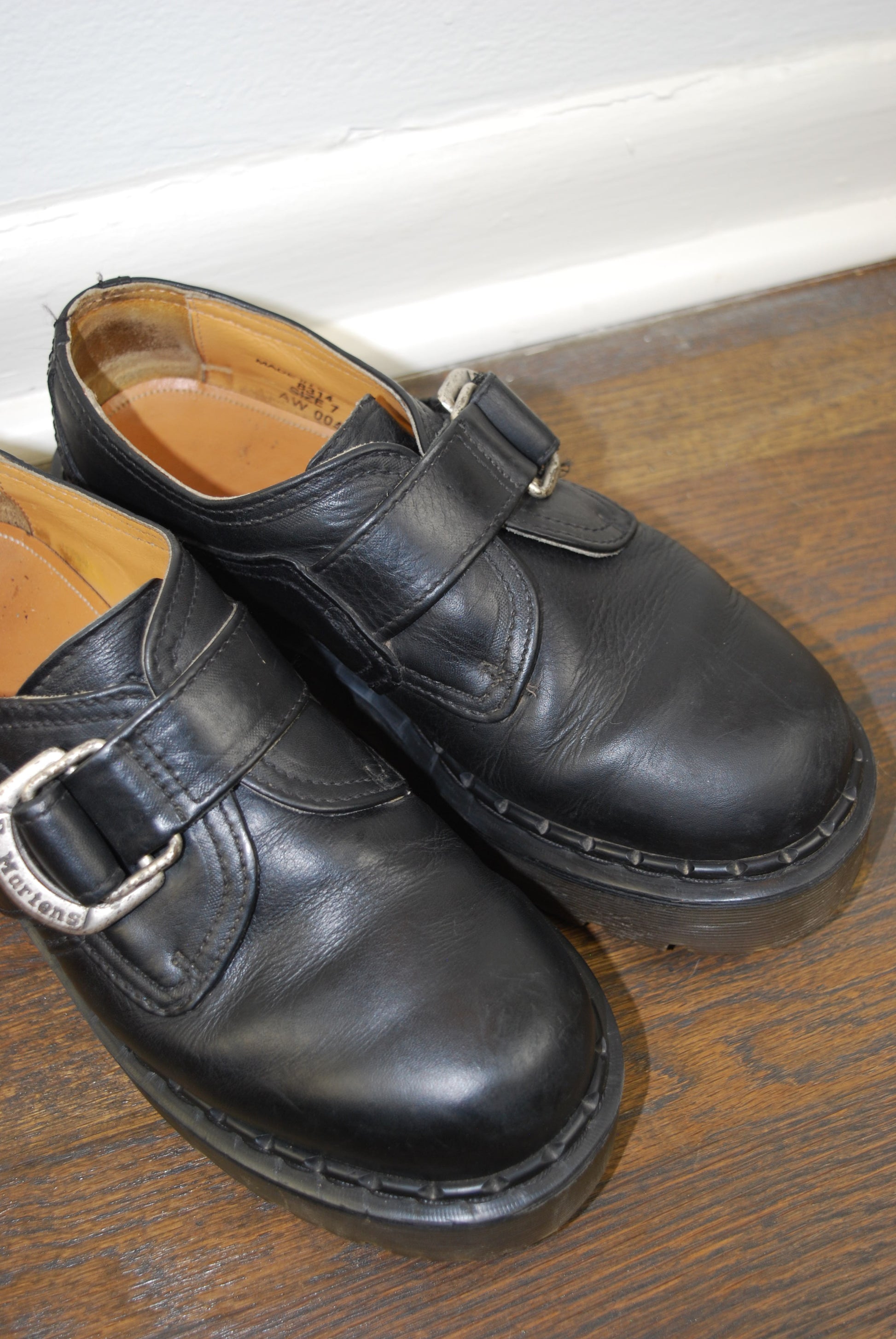 Pair of black leather shoes with buckles on a wooden surface