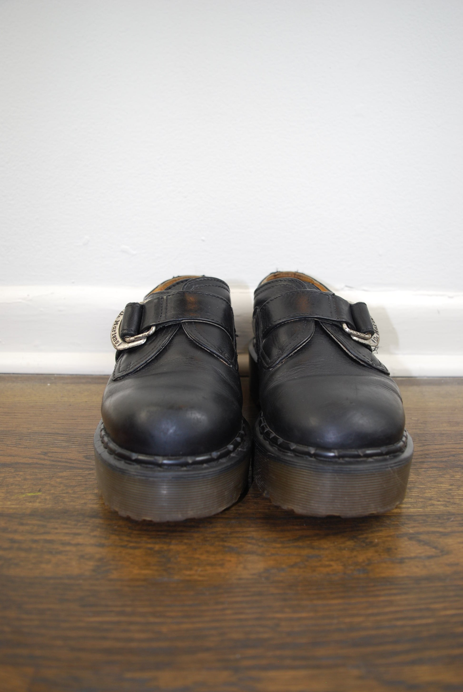 Pair of black leather shoes on a wooden floor with a white wall background