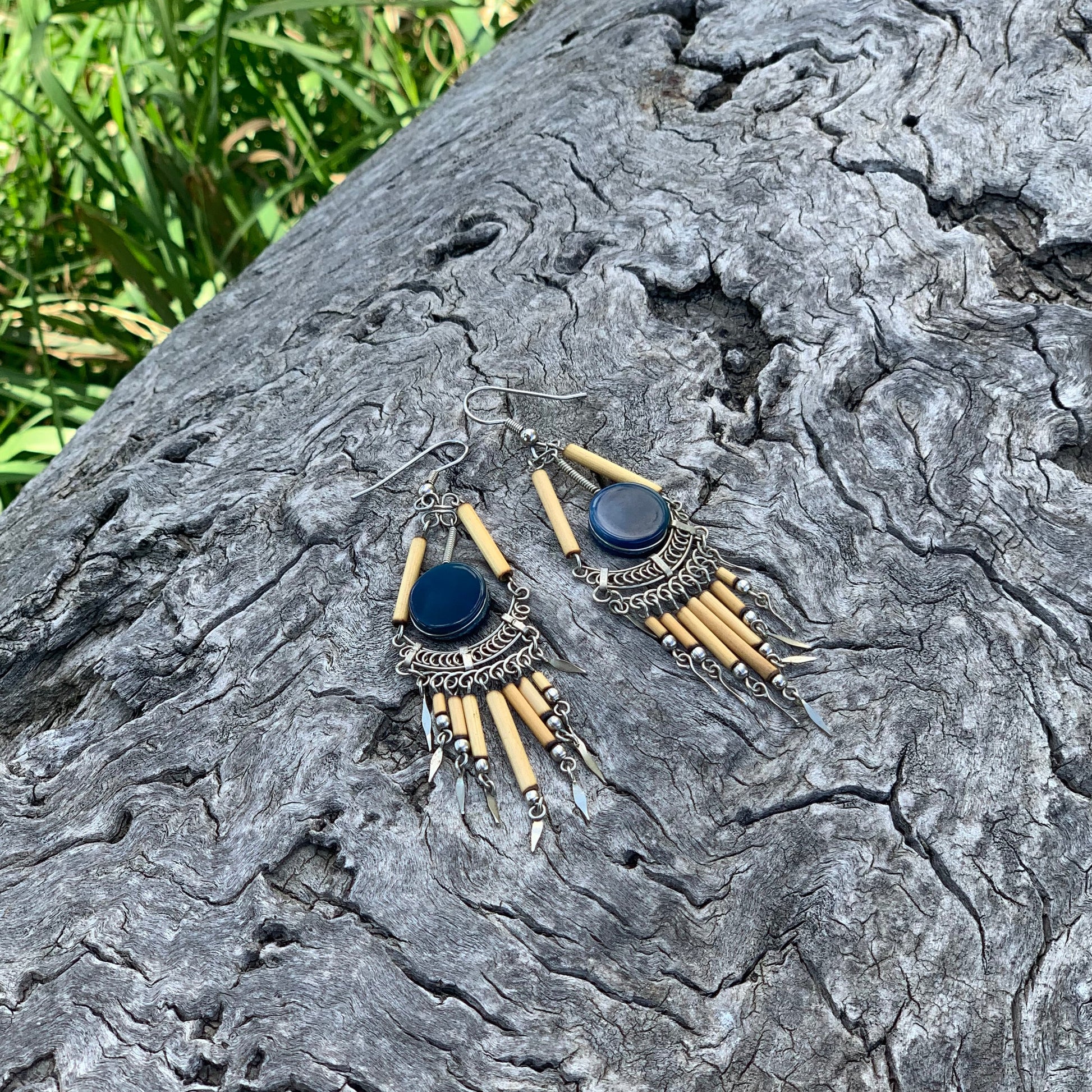 Pair of earrings on a textured stone surface with grass in the background