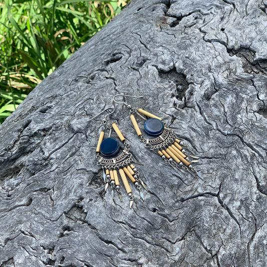 Pair of earrings on a textured stone surface with grass in the background