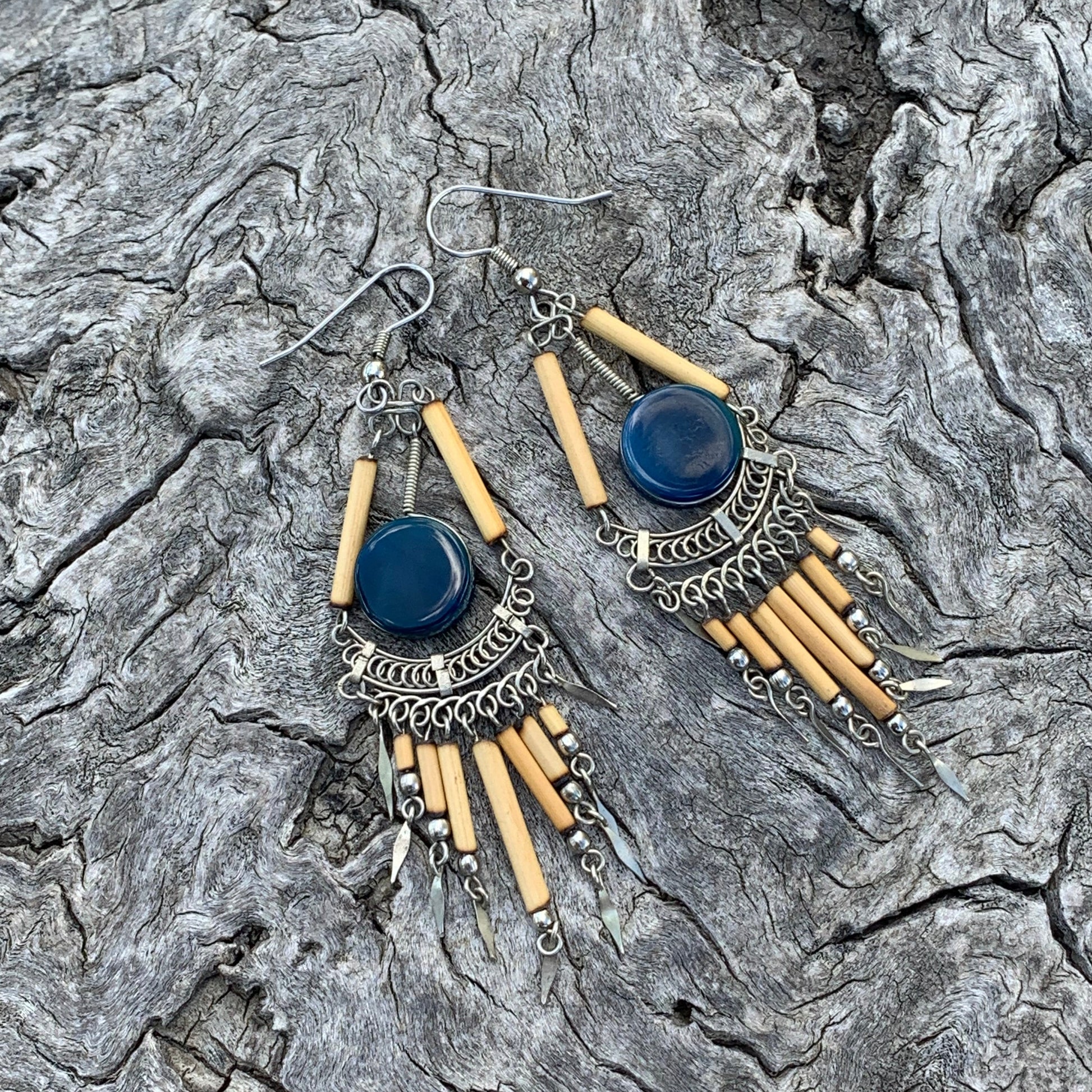 Pair of earrings with blue stones and beige cylindrical beads on a textured stone surface