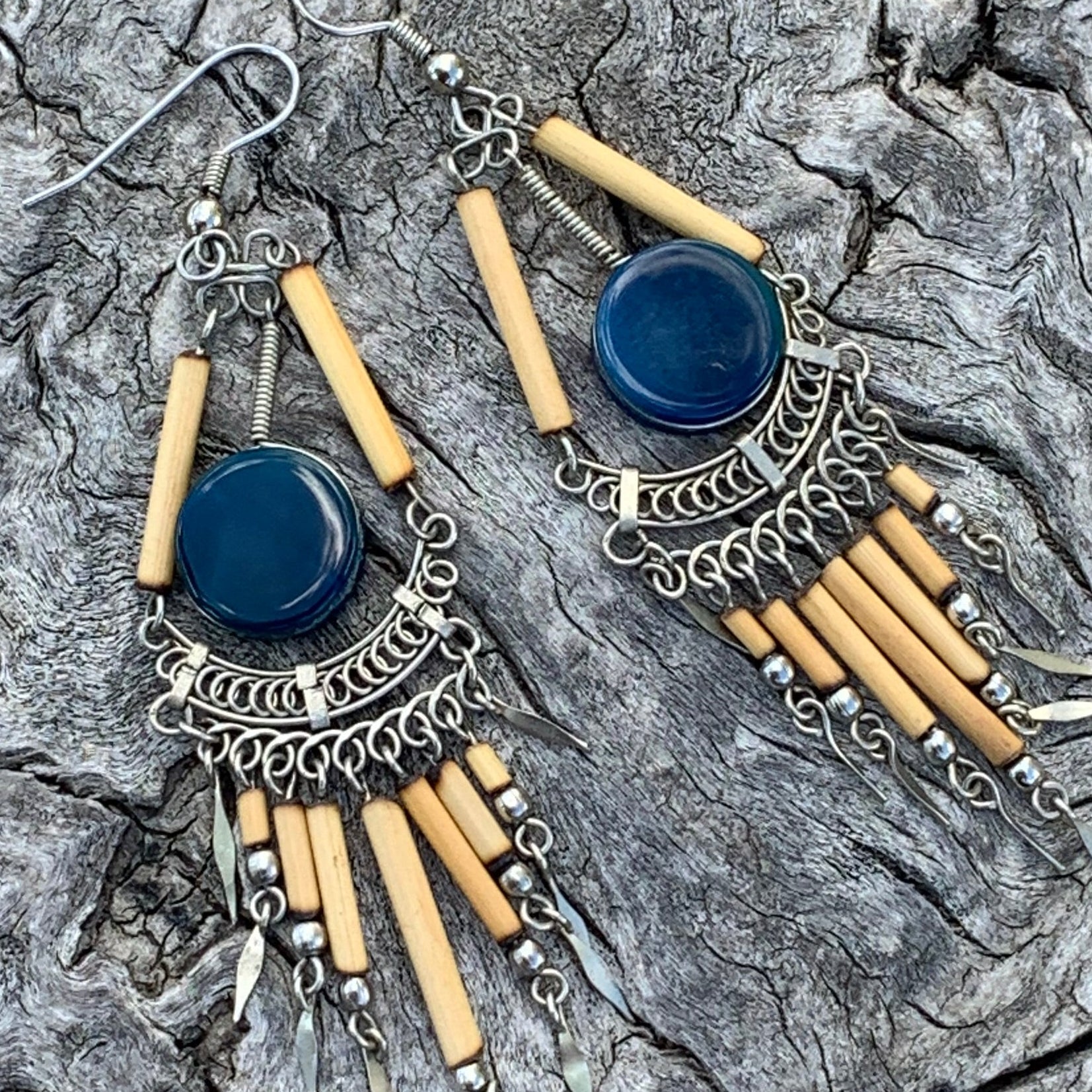 Pair of earrings with blue stones and beige sticks on a textured gray surface