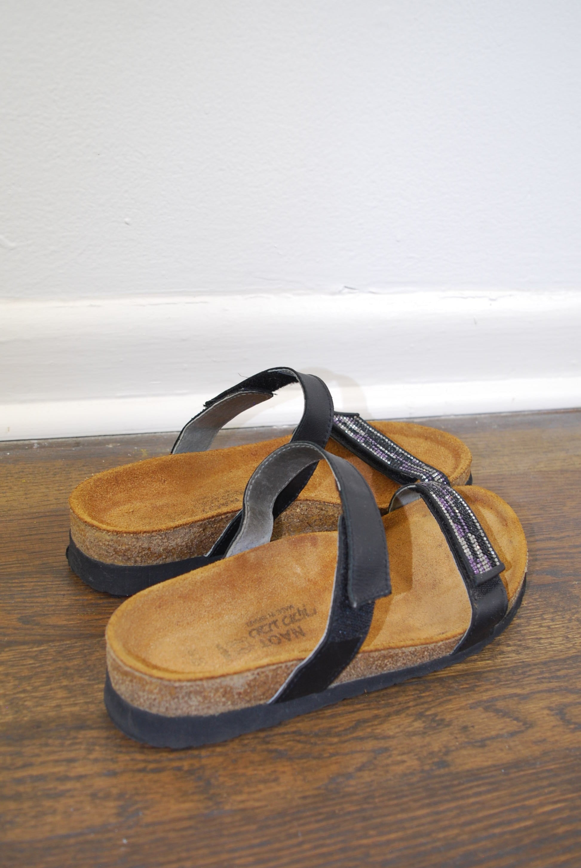 Pair of sandals with black straps on a wooden floor.