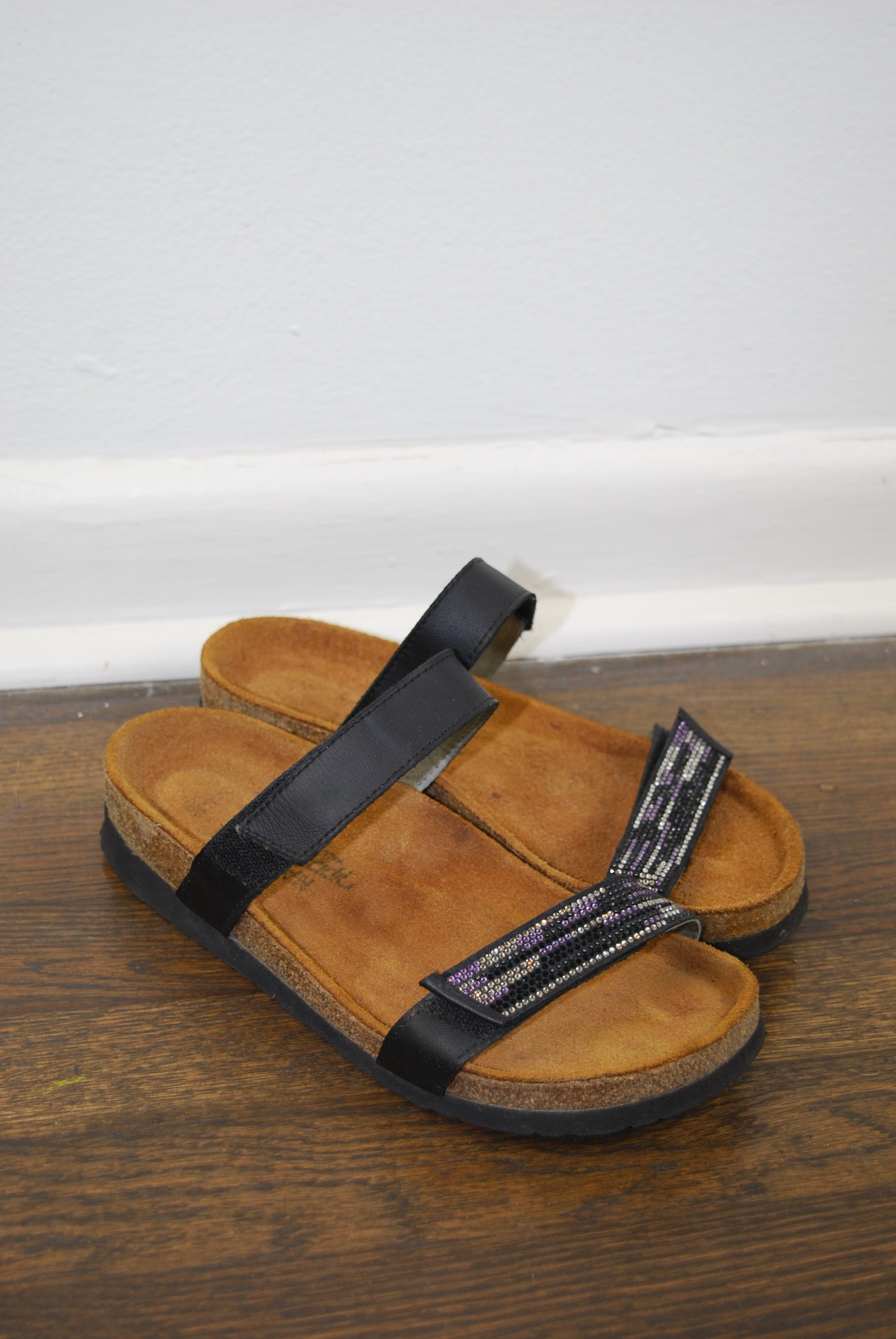 Pair of brown sandals with black straps on a wooden surface