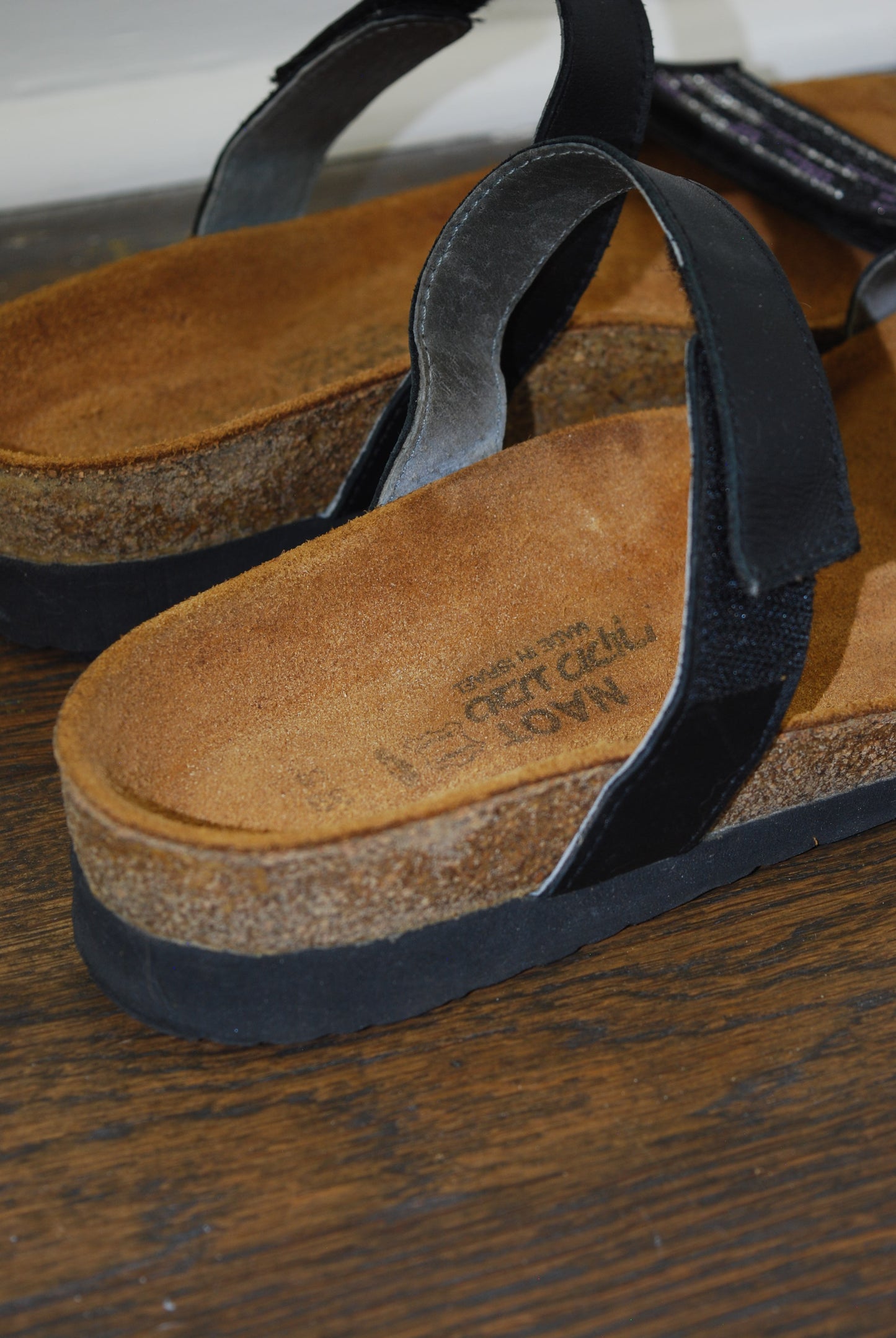 Close-up of a sandal with a visible brand logo on a wooden surface