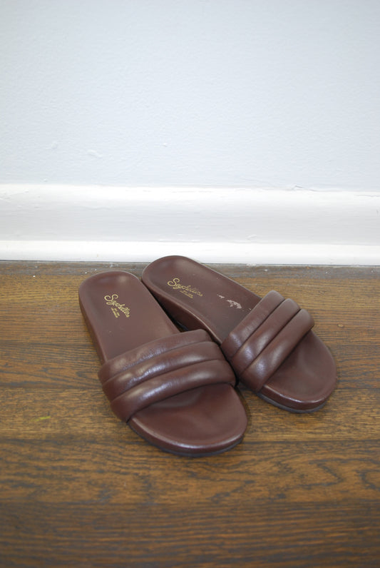 Pair of brown slides on a wooden surface with a white background
