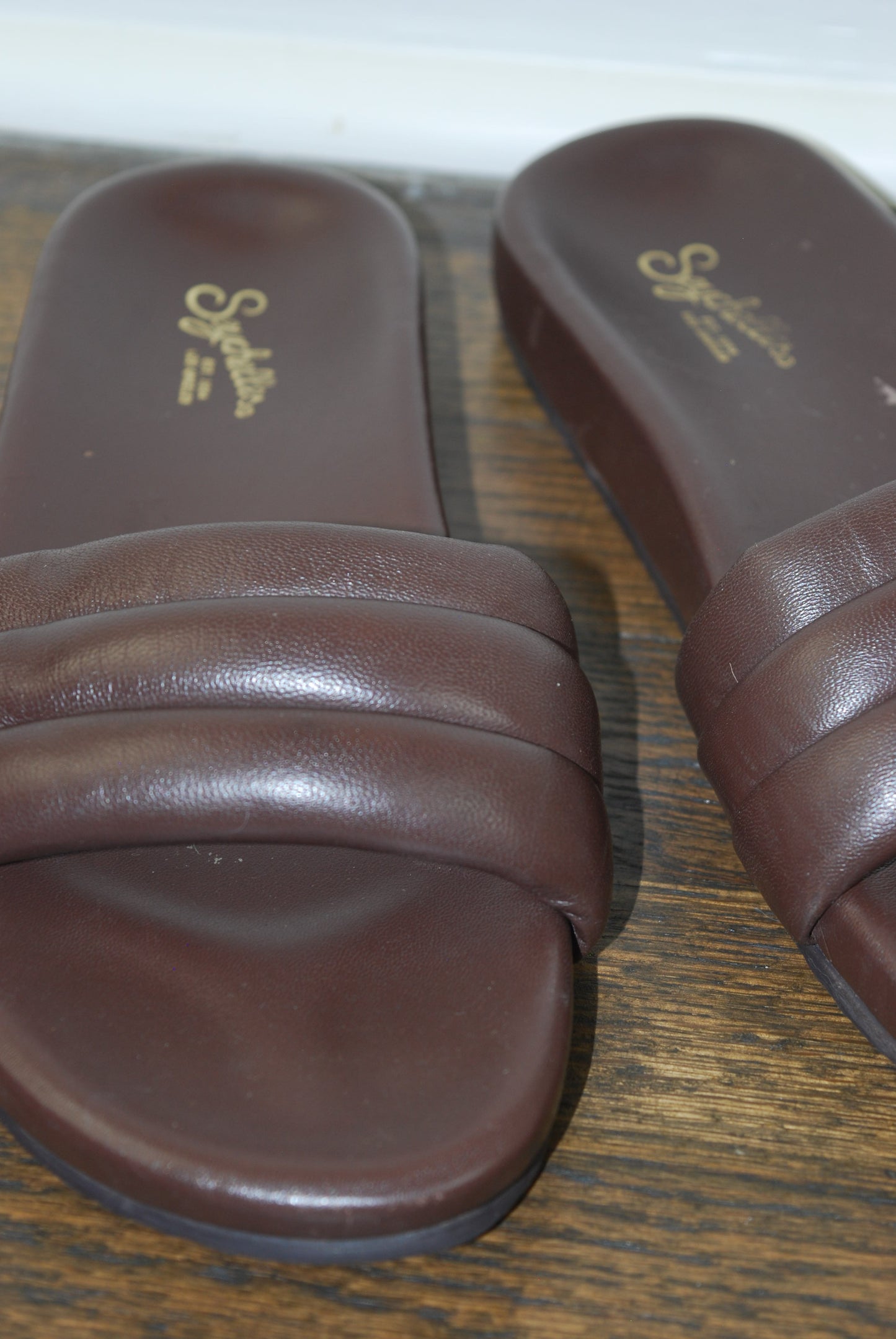 Pair of brown sandals with Seychelles logo on a wooden surface