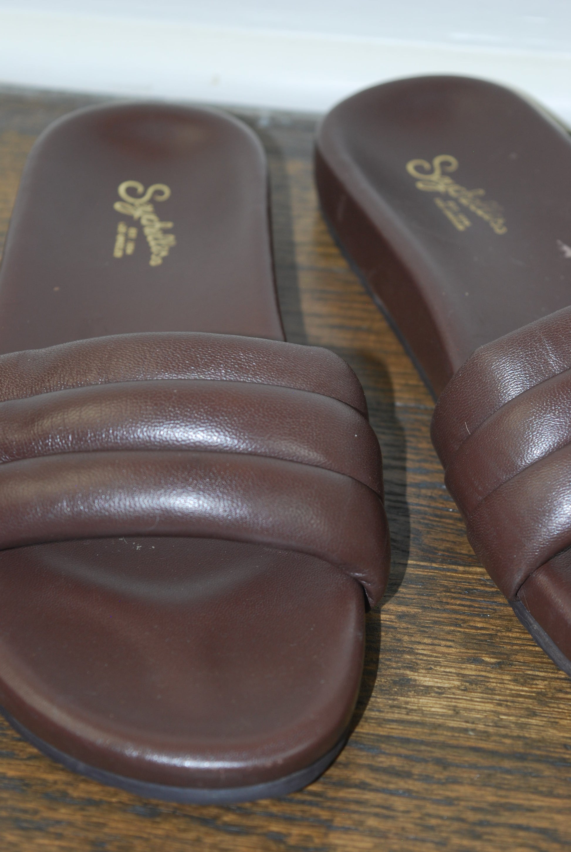 Pair of brown sandals with Seychelles logo on a wooden surface