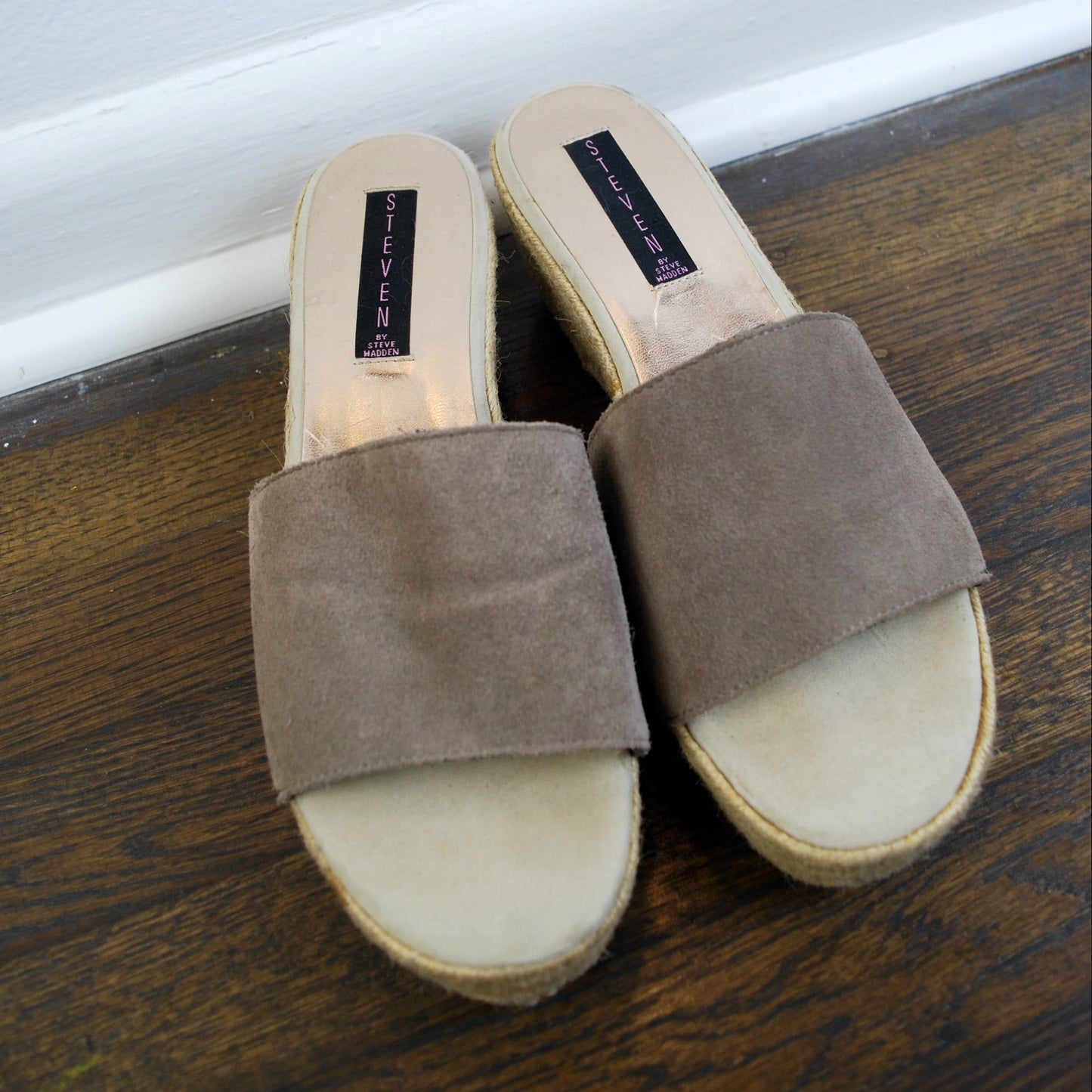 Pair of brown suede slides on a wooden floor.