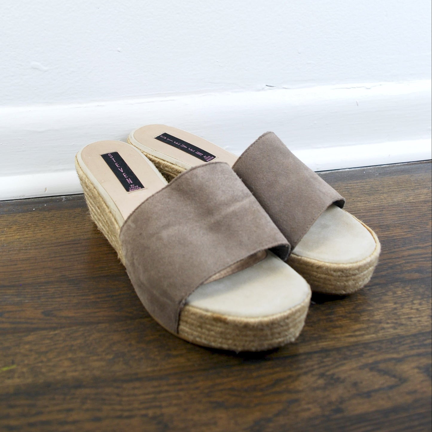 Pair of brown suede sandals with wooden soles on a wooden floor.
