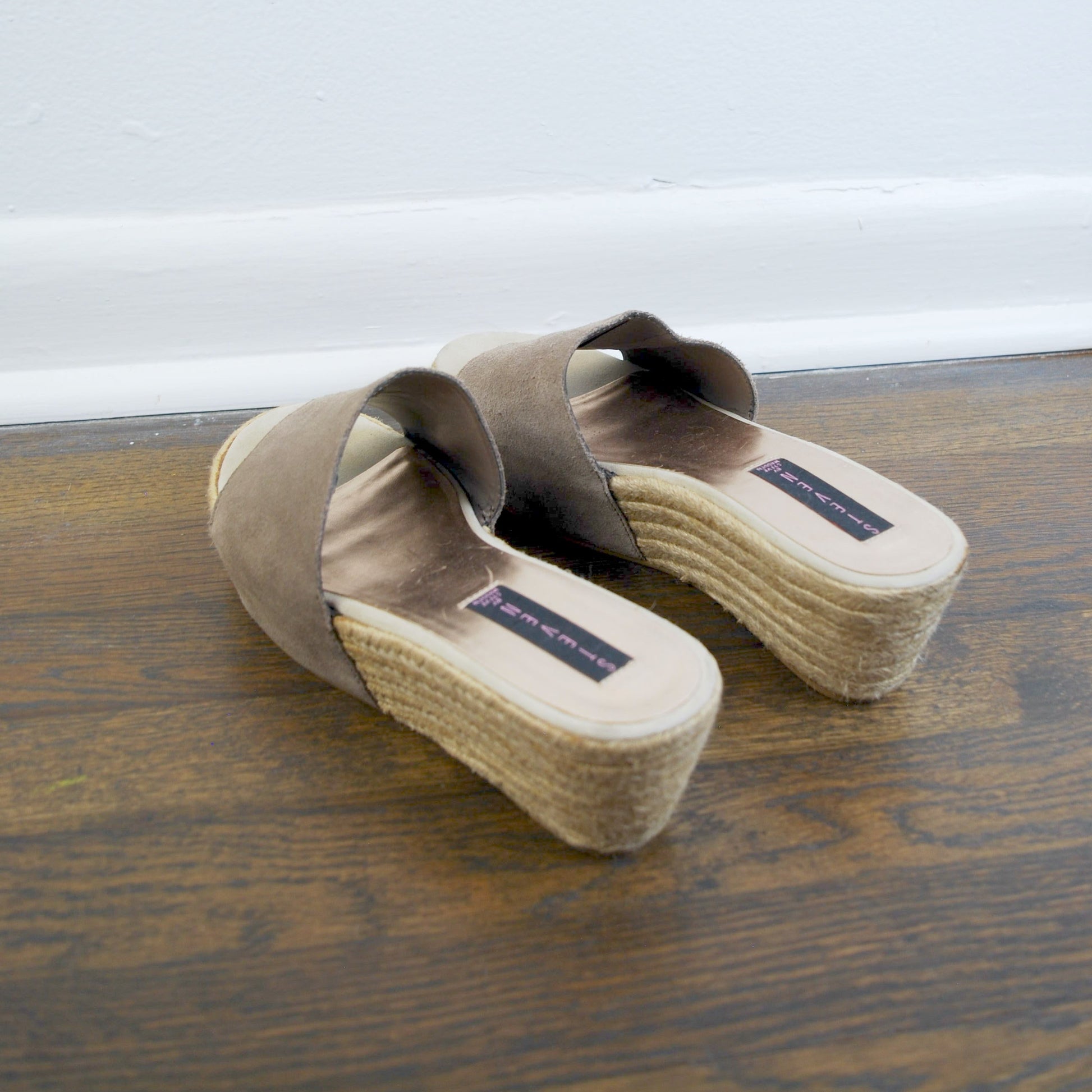 Pair of brown sandals with jute soles on a wooden floor.