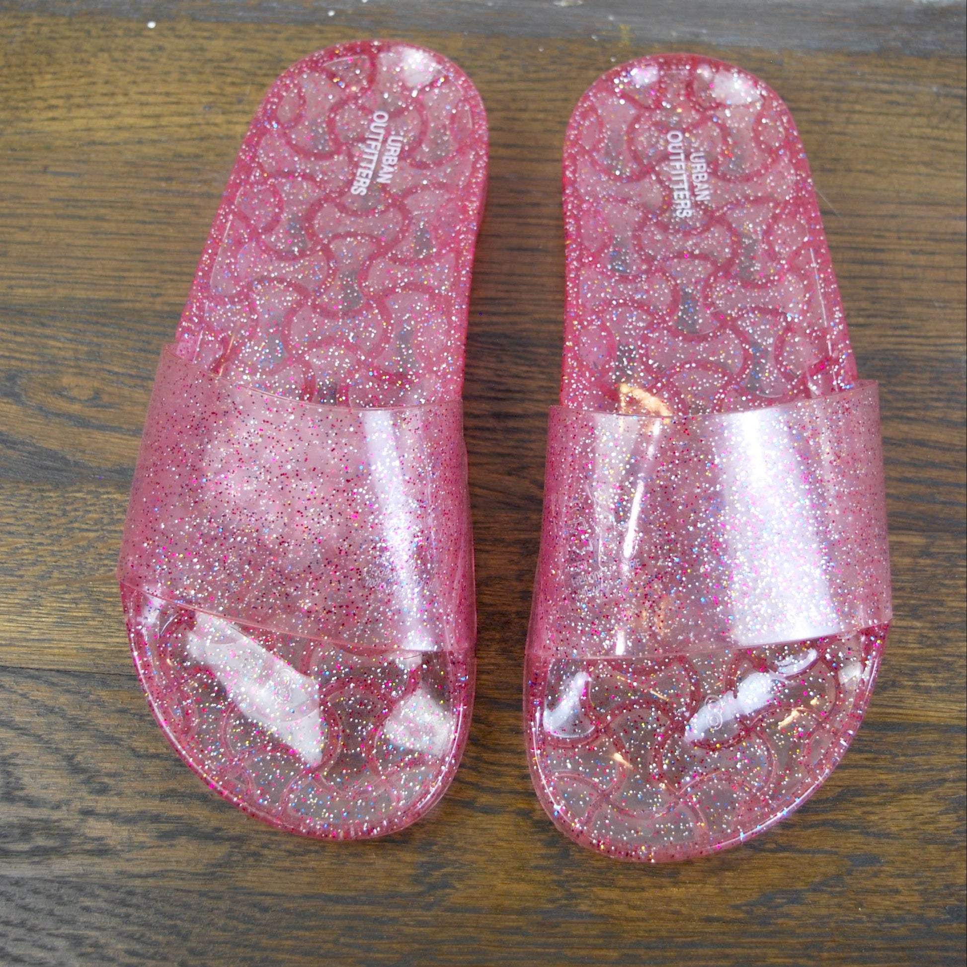 Pair of pink glittery slides on a wooden floor