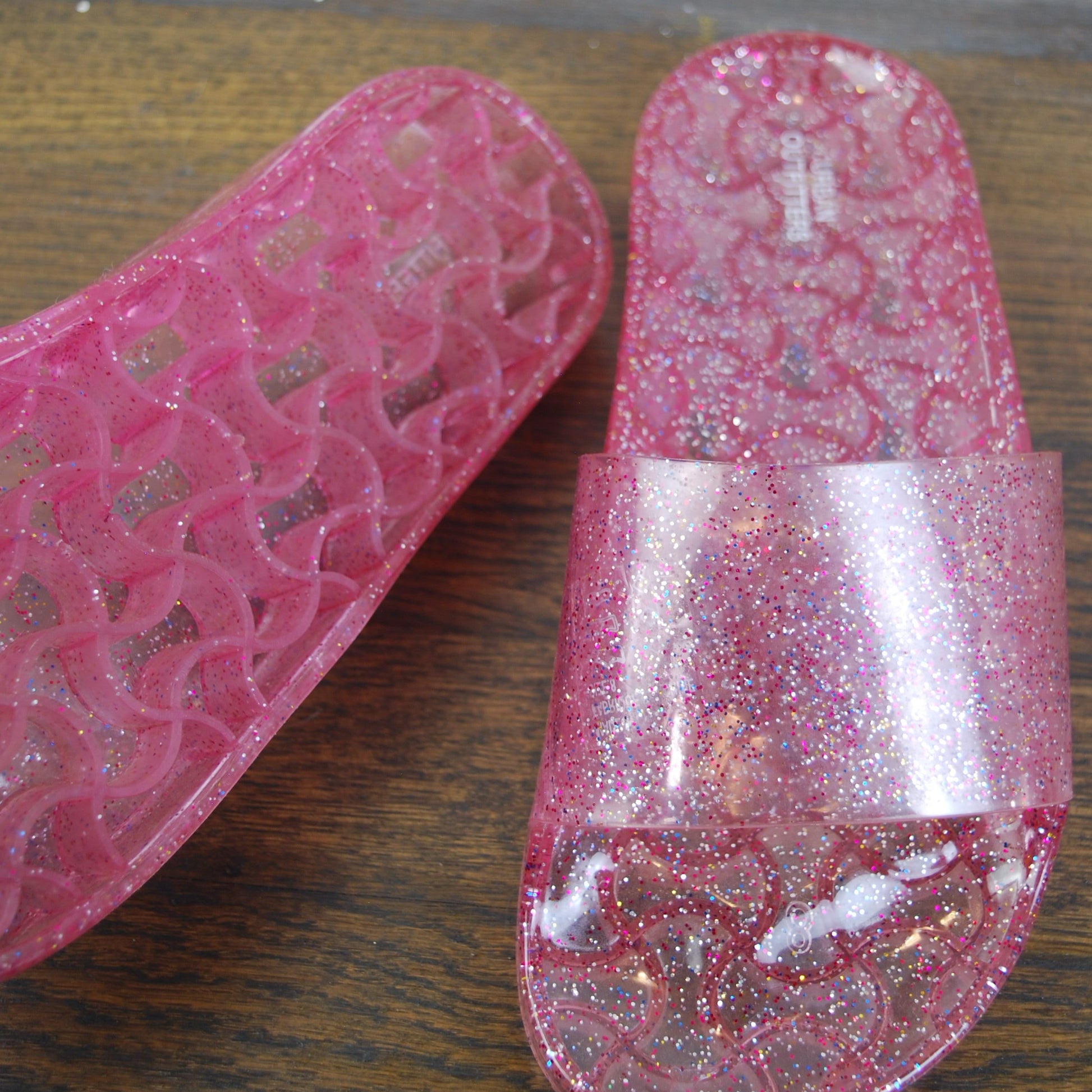 Pink glittery slide sandals on a wooden surface