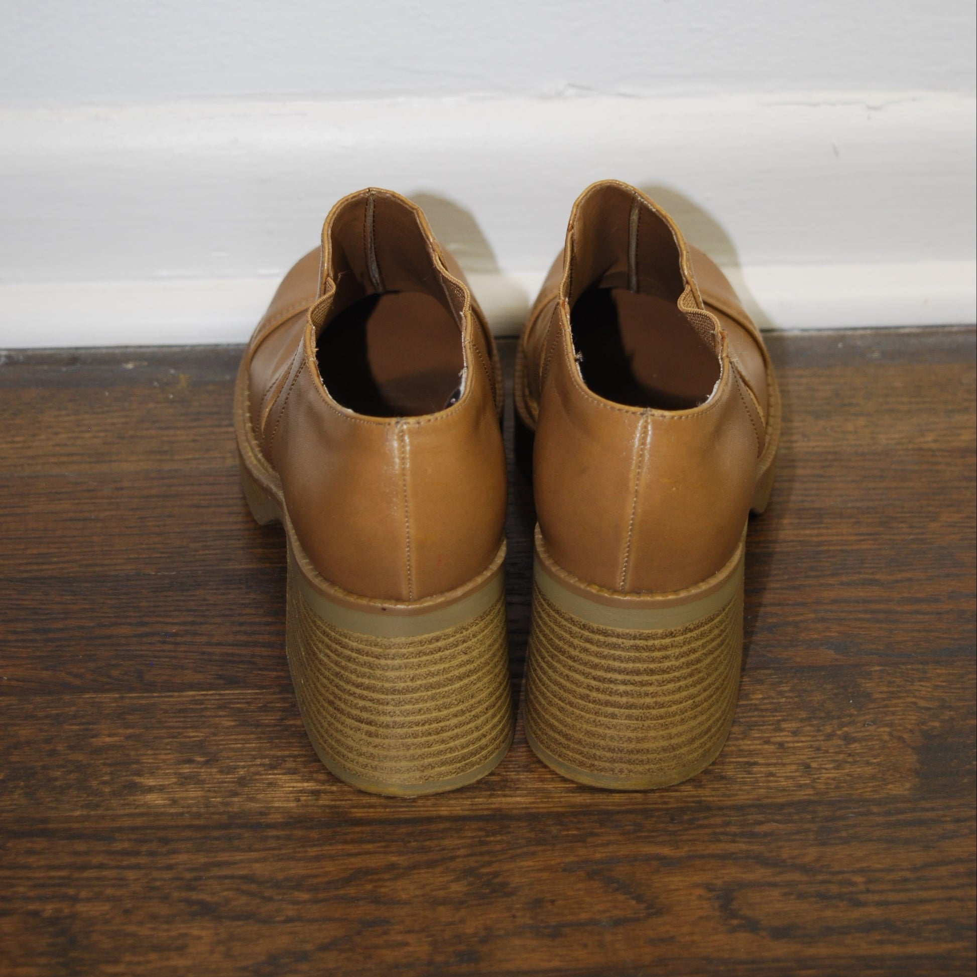 Pair of brown shoes on a wooden surface with a white background