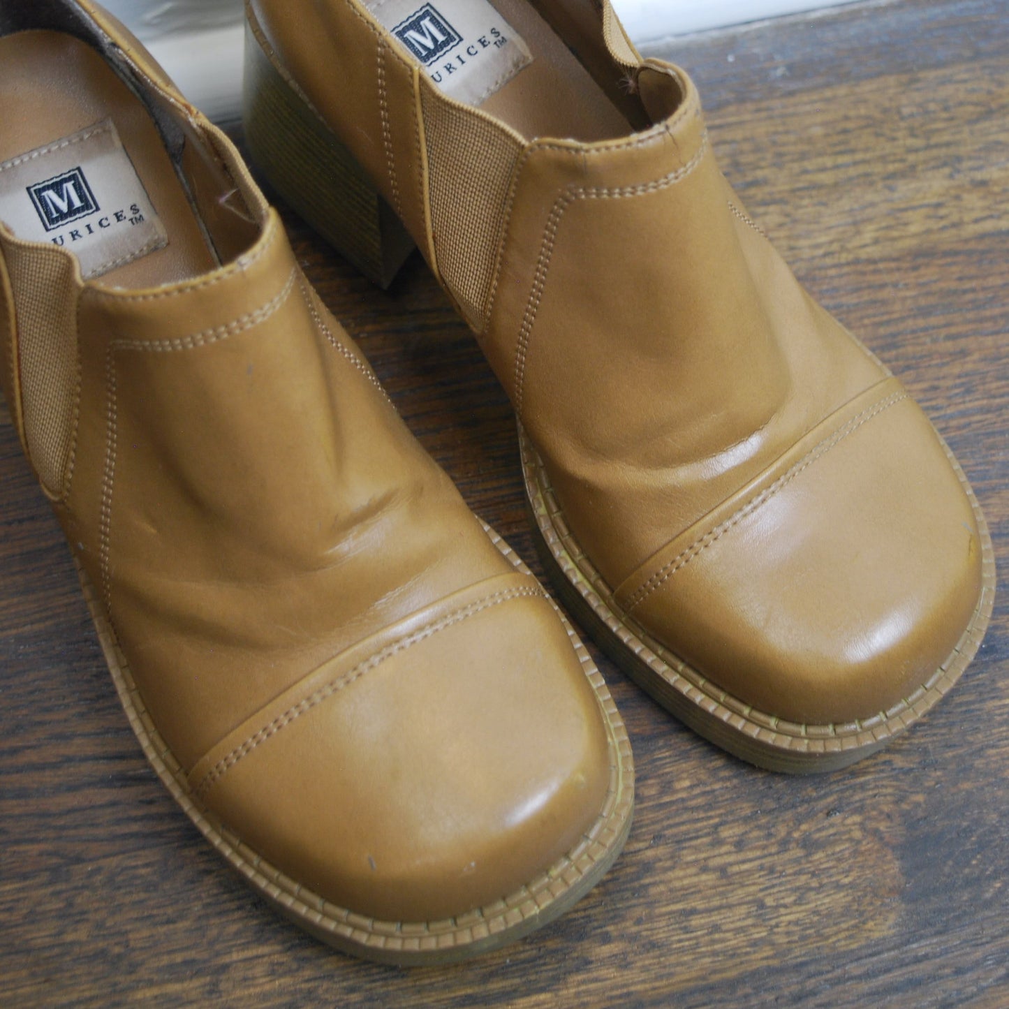 Pair of tan shoes on a wooden floor with a white baseboard.